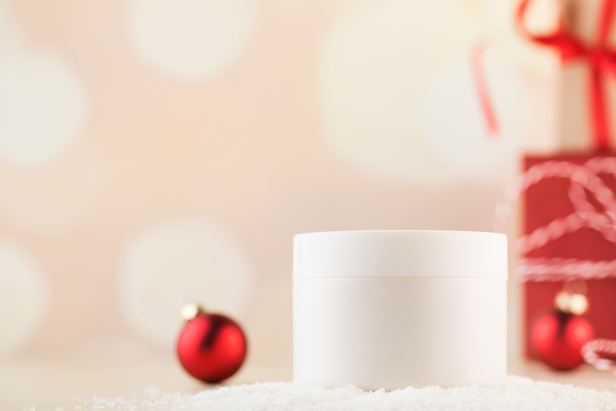 A white jar with nourishing cream for face and body in the snow with Christmas balls