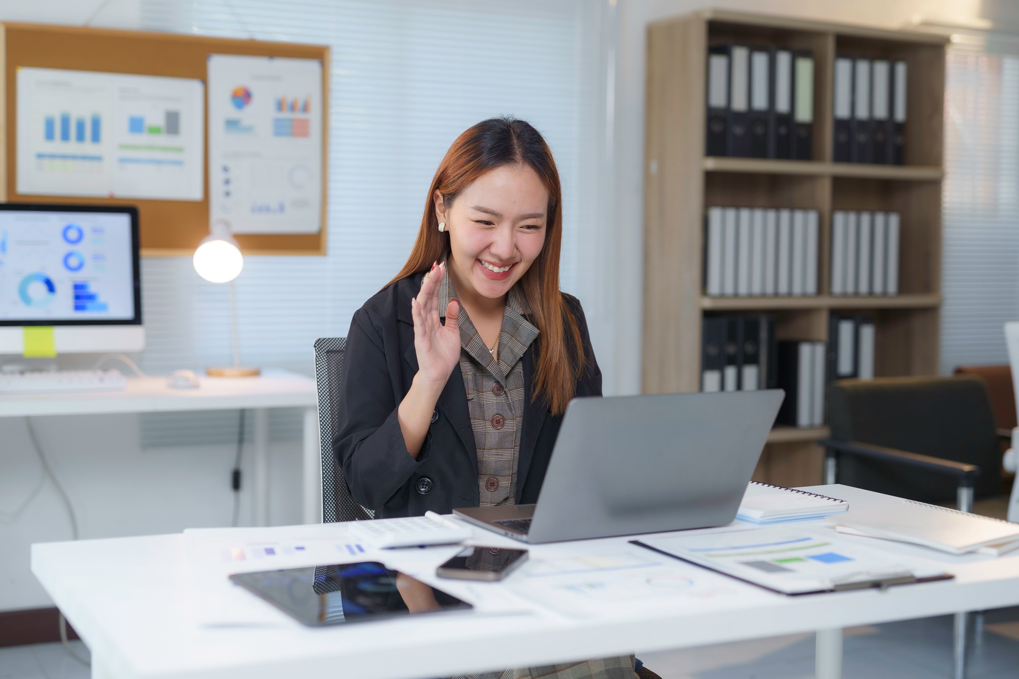 Asian businesswoman waving during video conference in modern office
