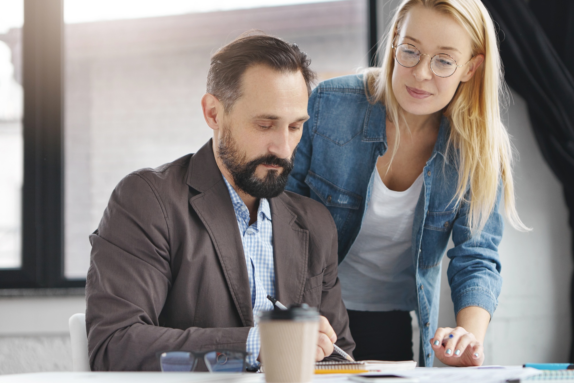 Bearded male manager in formal suit and his female assistant prepare together forecast of marketing,