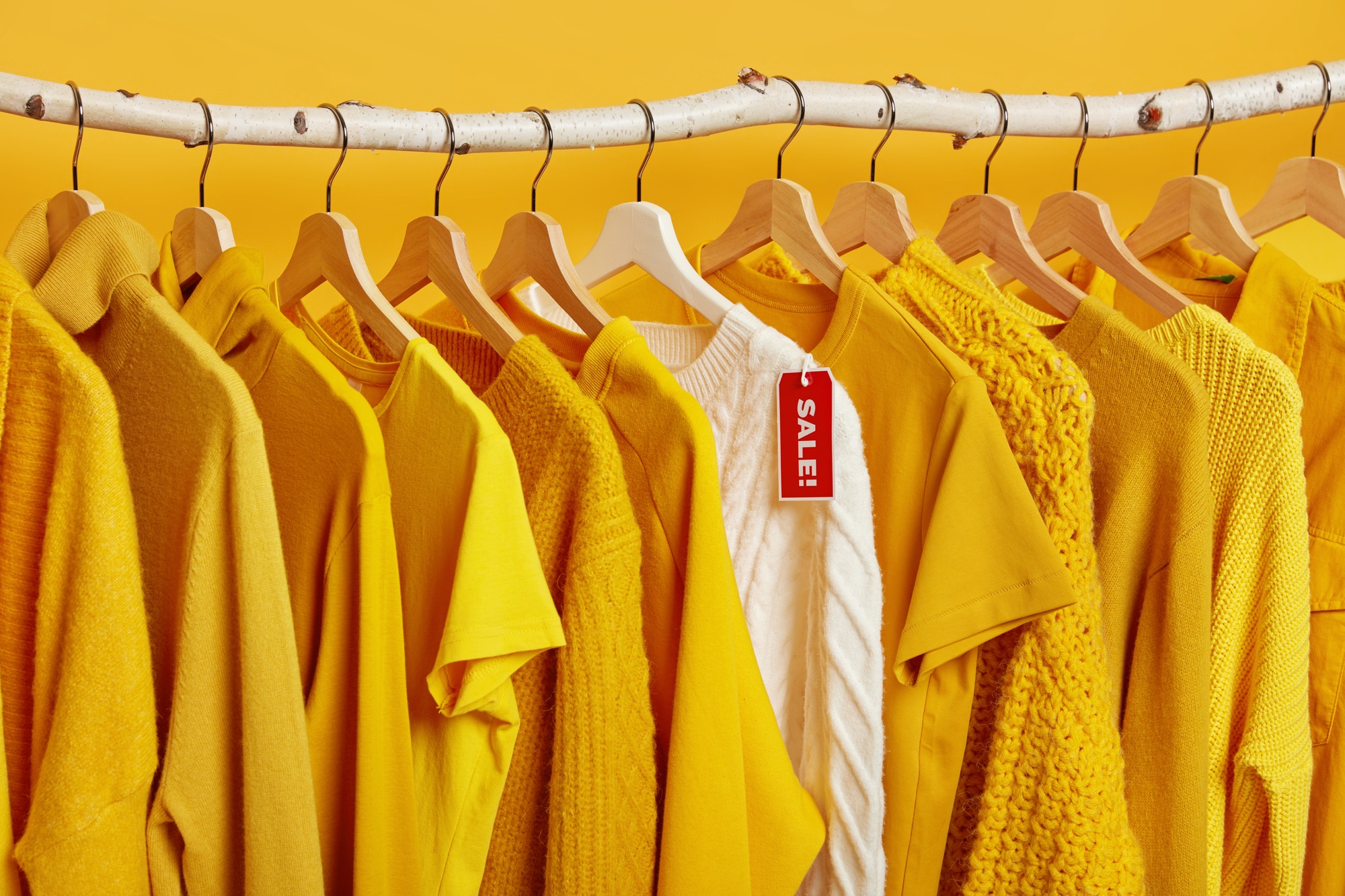 Clearance sale in clothes store. Yellow and bright clothing on hangers during Black Friday. Big disc