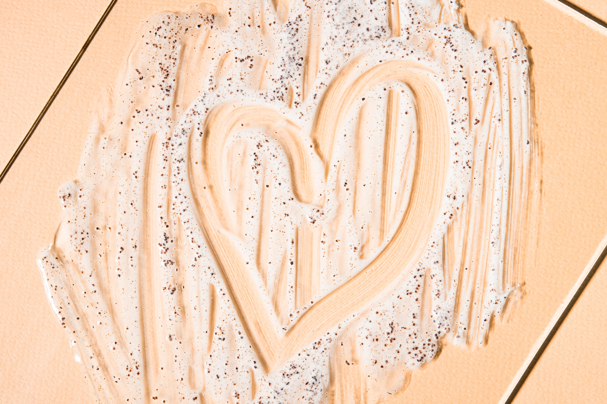 Cosmetic product applied in the shape of a heart on a beige background, top view.