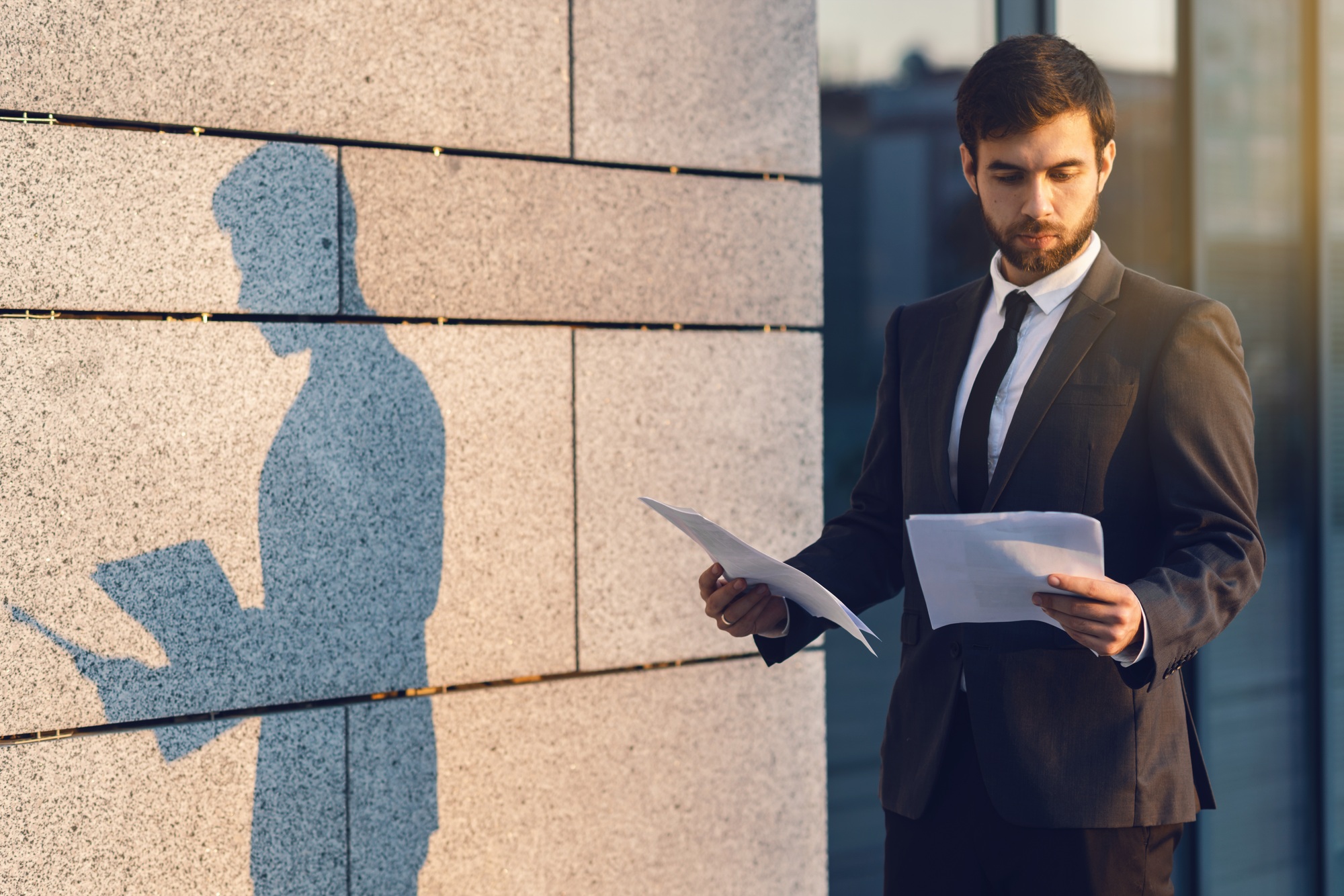 Serious young businessman in a classic suit reading advantageous business document in paper form