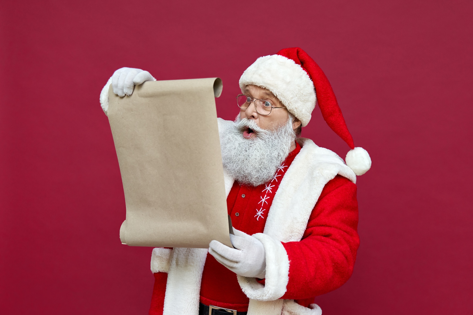 Shocked Santa Claus wearing costume reading wish list on red background.