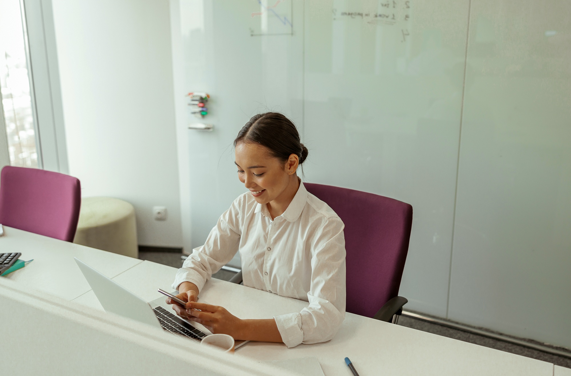 Smiling asian business woman sitting in meeting room before conference and holding phone