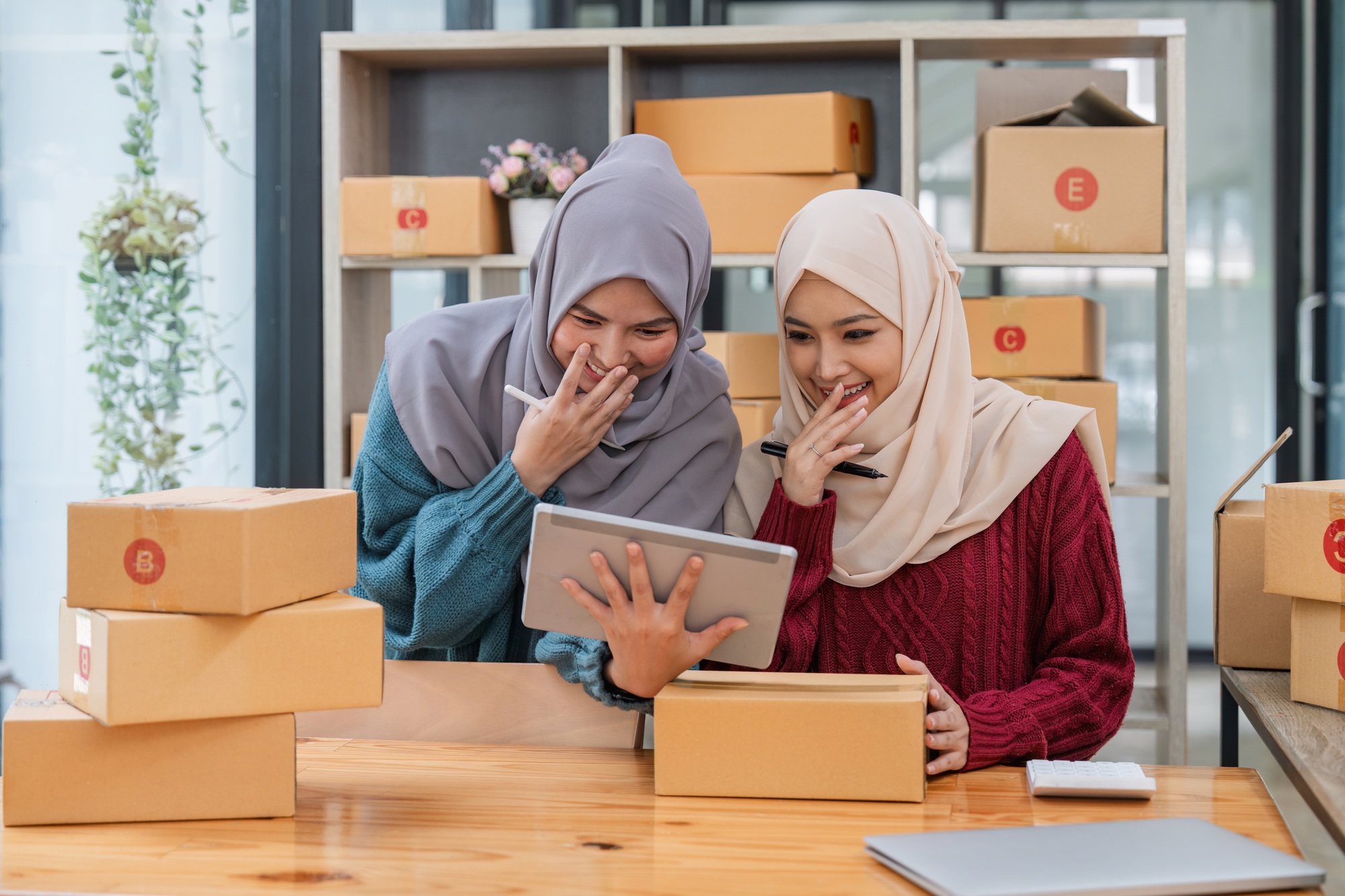 Two women muslim look at online product sales data on laptops and tablet surprised joy