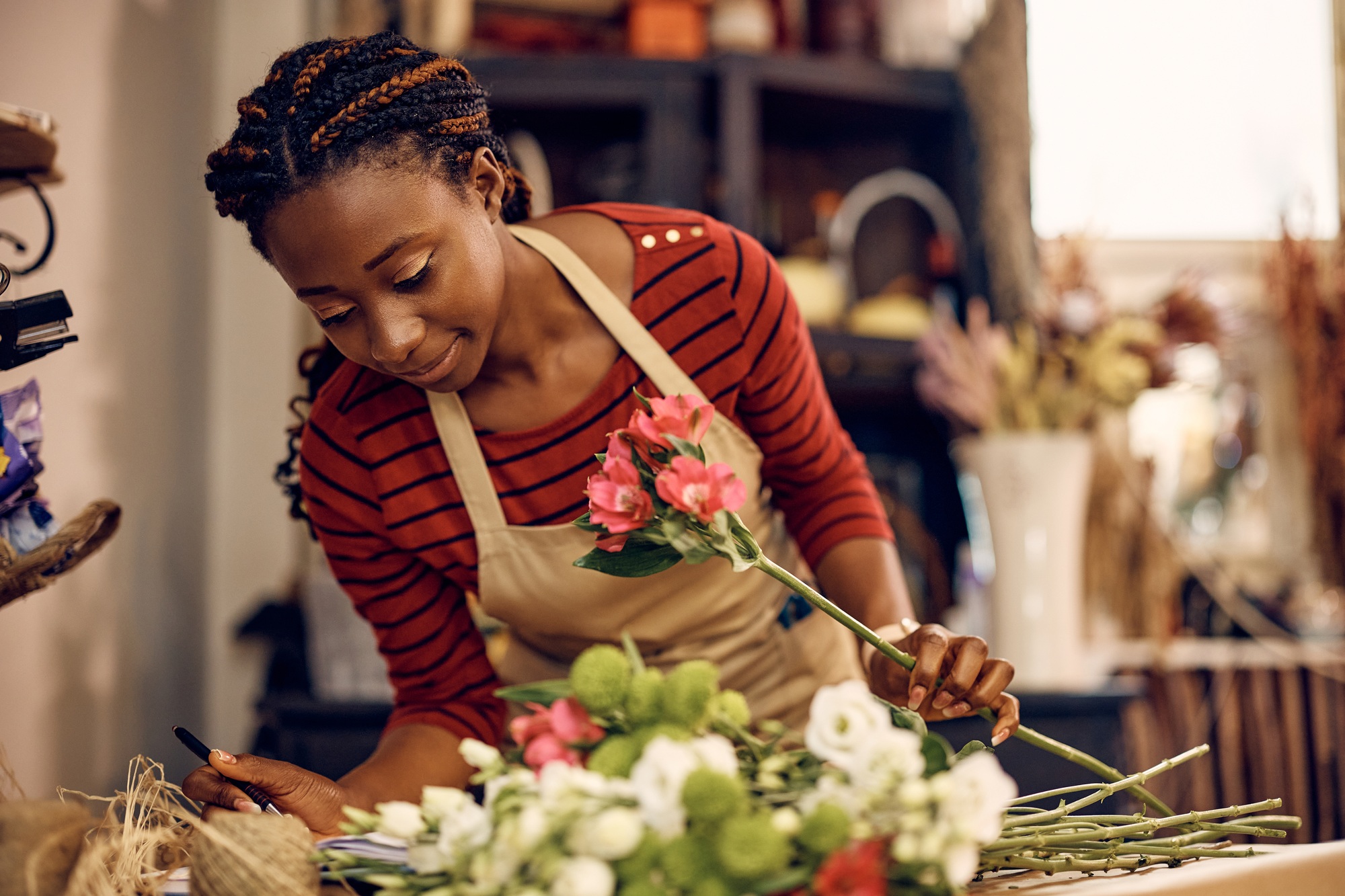 Young black woman making custom made bouquet of flowers at floral workshop.