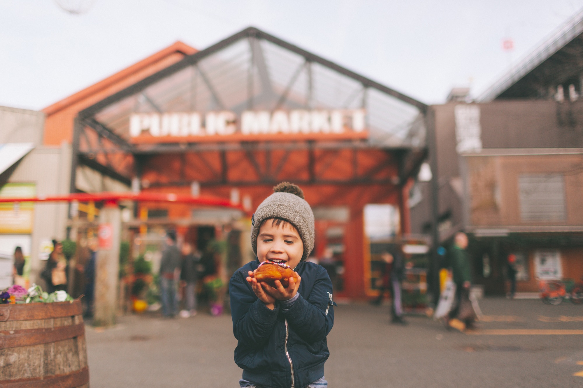 A little boy happily eating a donut in front of a public market.