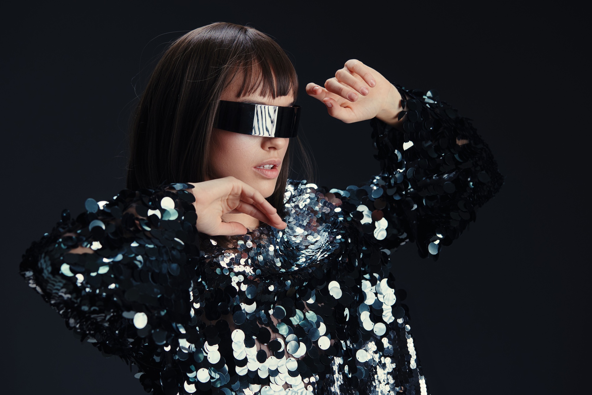 A stylish woman in sunglasses and a sequinned shirt stands confidently with hands on her hips and