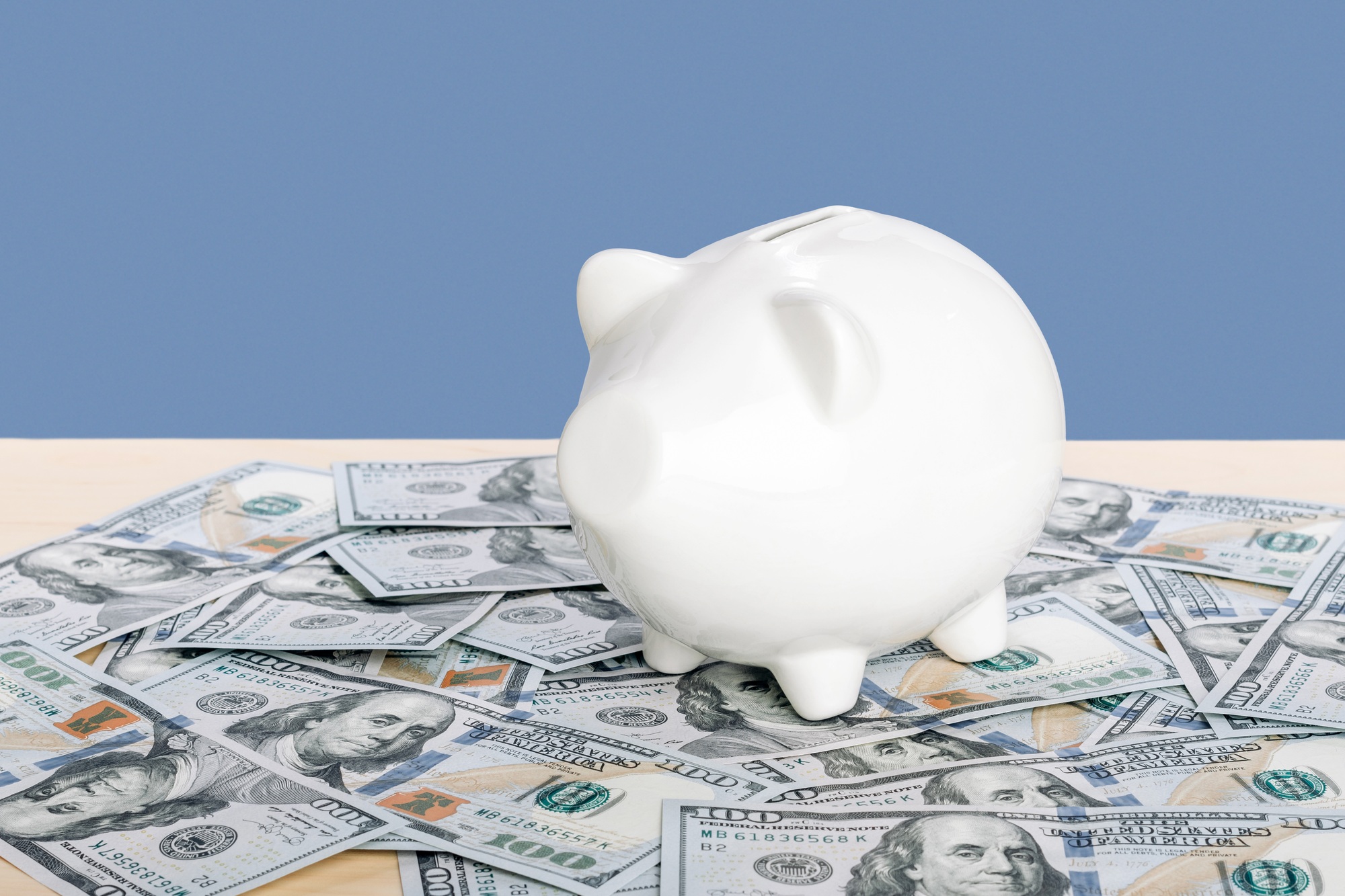 A white piggy bank stands on pile of hundred dollar bills. Wealth and prosperity concept