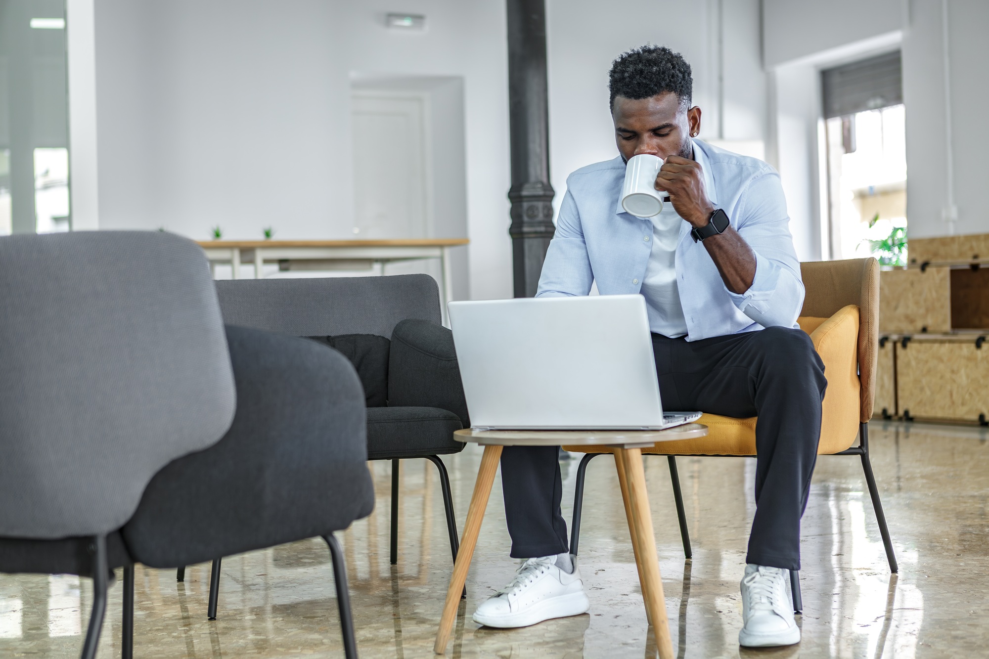 A young man working on a laptop while enjoying coffee in a modern coworking space