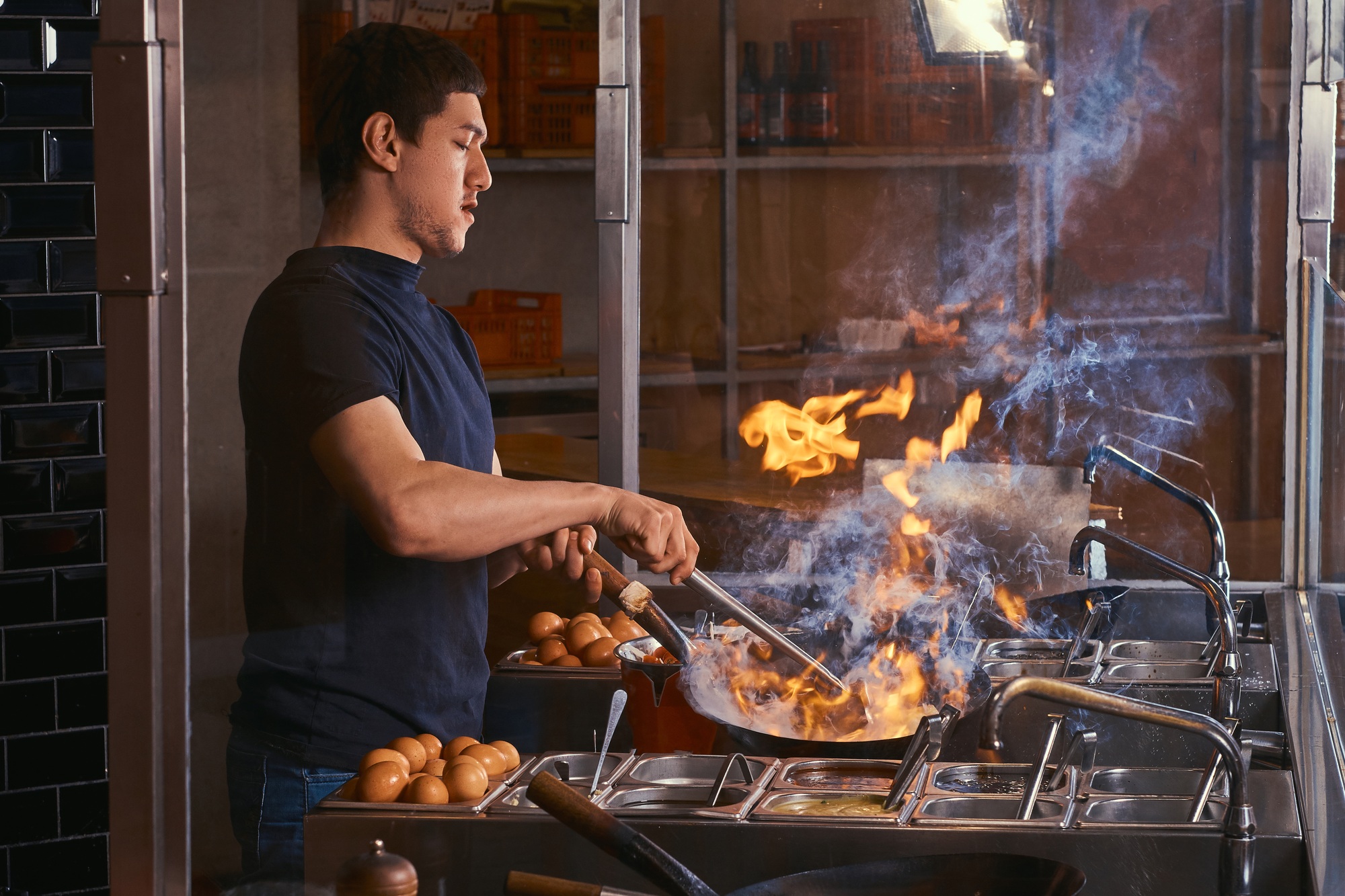 Cooking process in an Asian restaurant. Cook is fry vegetables with spices and sauce in a wok