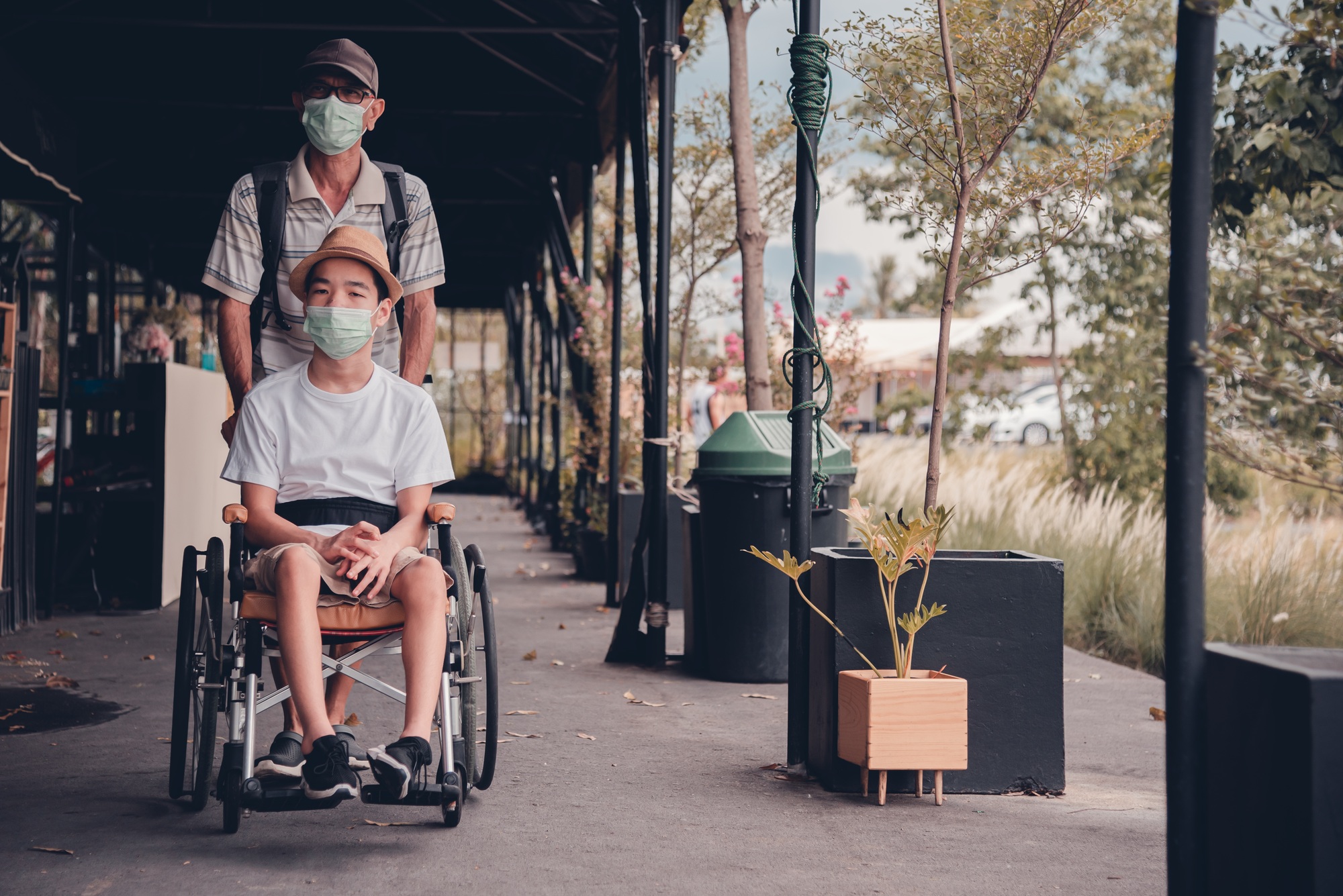 Disabled child on wheelchair and parent wearing a mask on the public market .