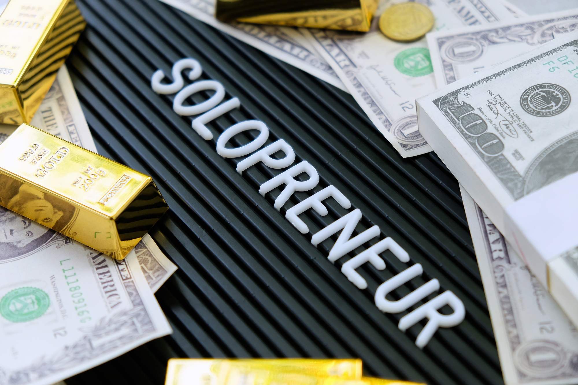 Gold bars and dollars on a black background with the word solopreneur.