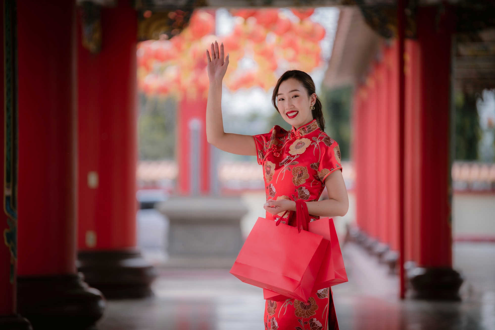 Happy Asian woman wearing red traditional cheongsam qipao dress holding shopping bags happiness in b