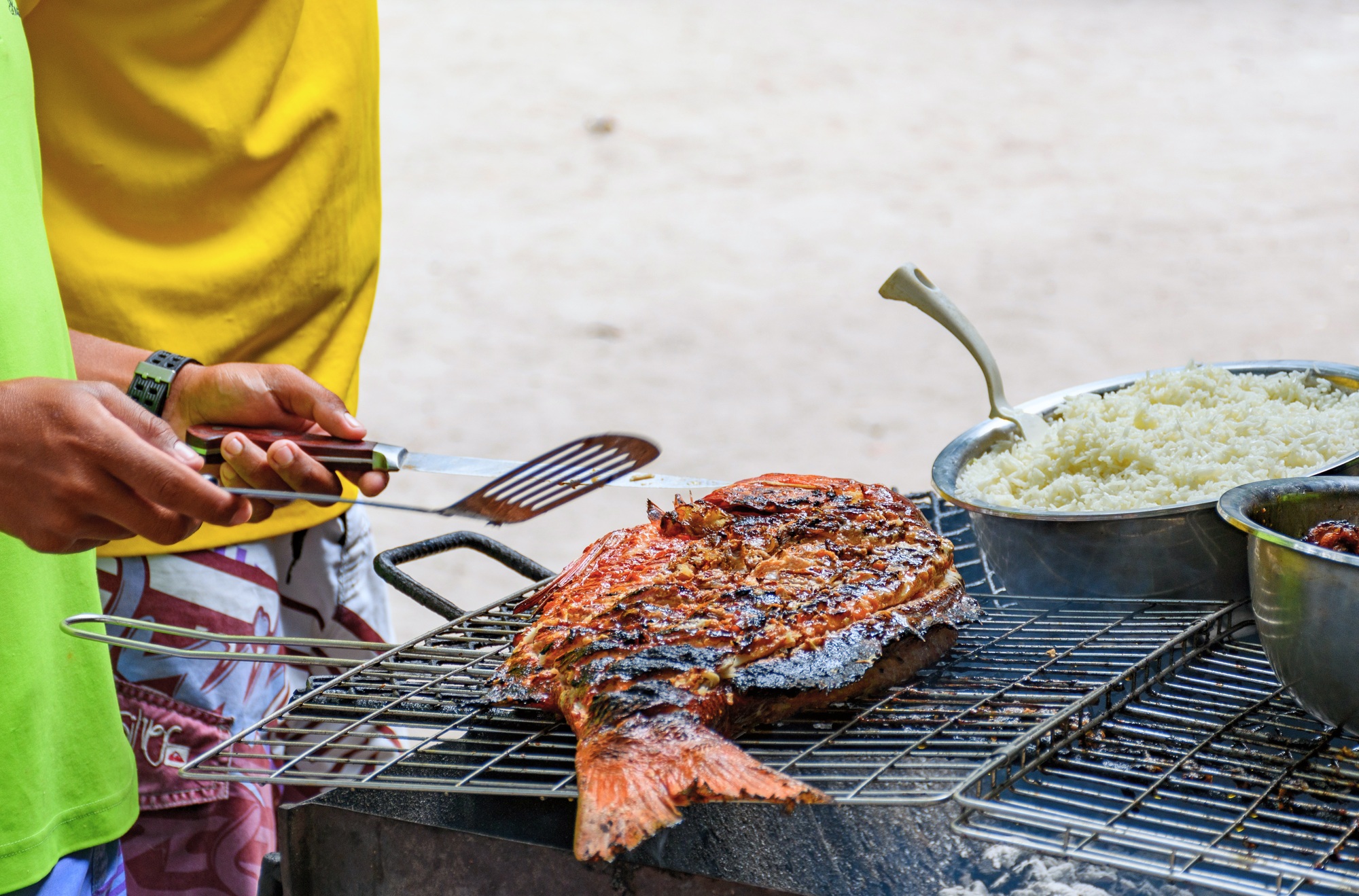 Large fish on grill. Person holding utensils, local food, local cuisine, seafood.