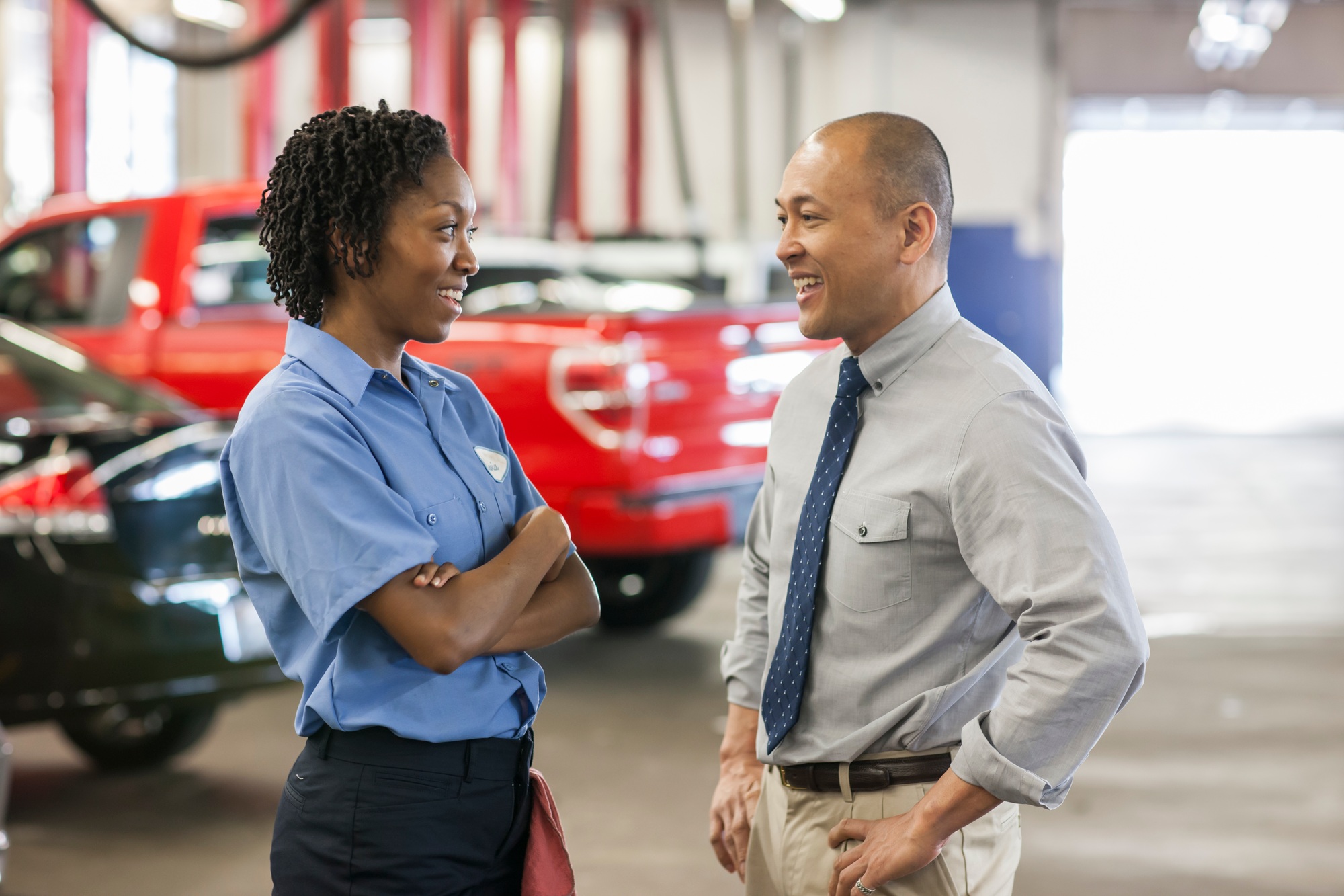 Male Pacific Islander auto repair shop manager talks to female Hispanic mechanic