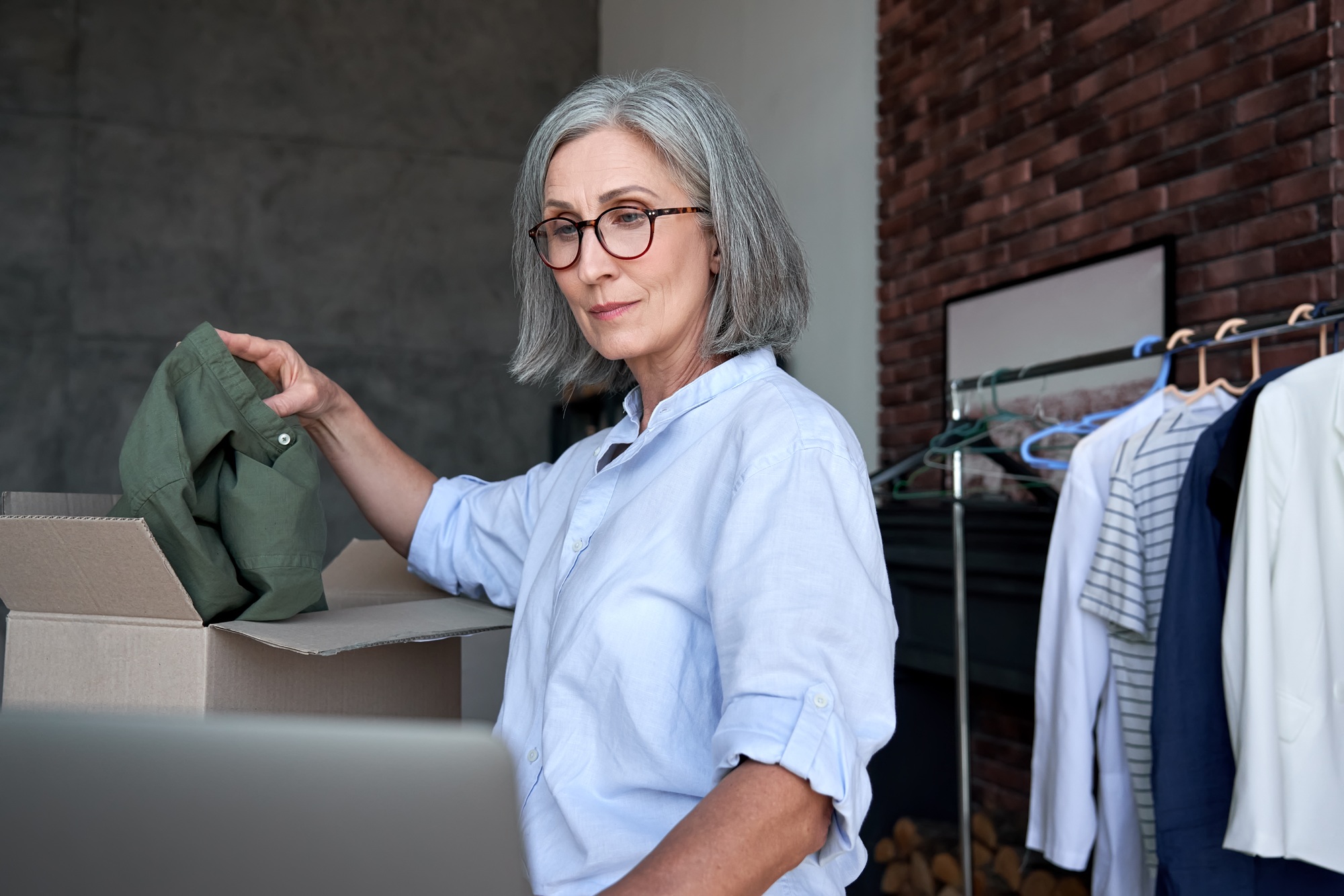 Older female dropshipping clothing business owner pack order in shipping box.