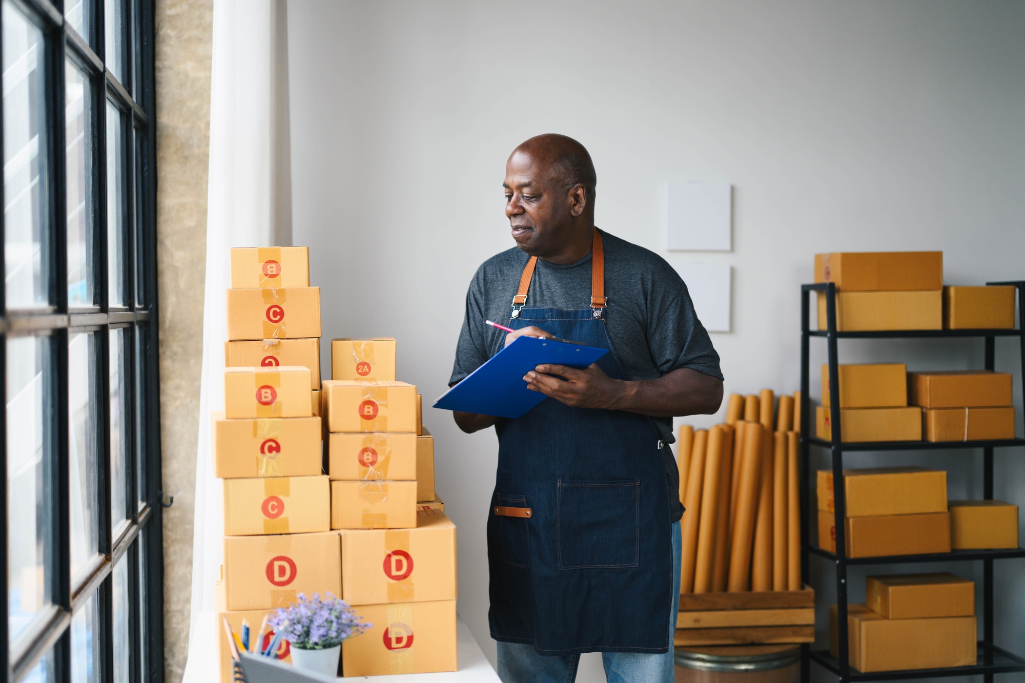 Small Business Owner Checking Inventory in Modern Workspace with Cardboard Boxes and Shelving Units