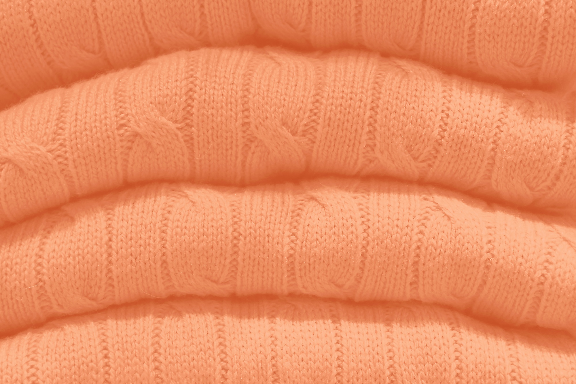 Stack of sweaters in trending color of year 2024 Peach Fuzz.