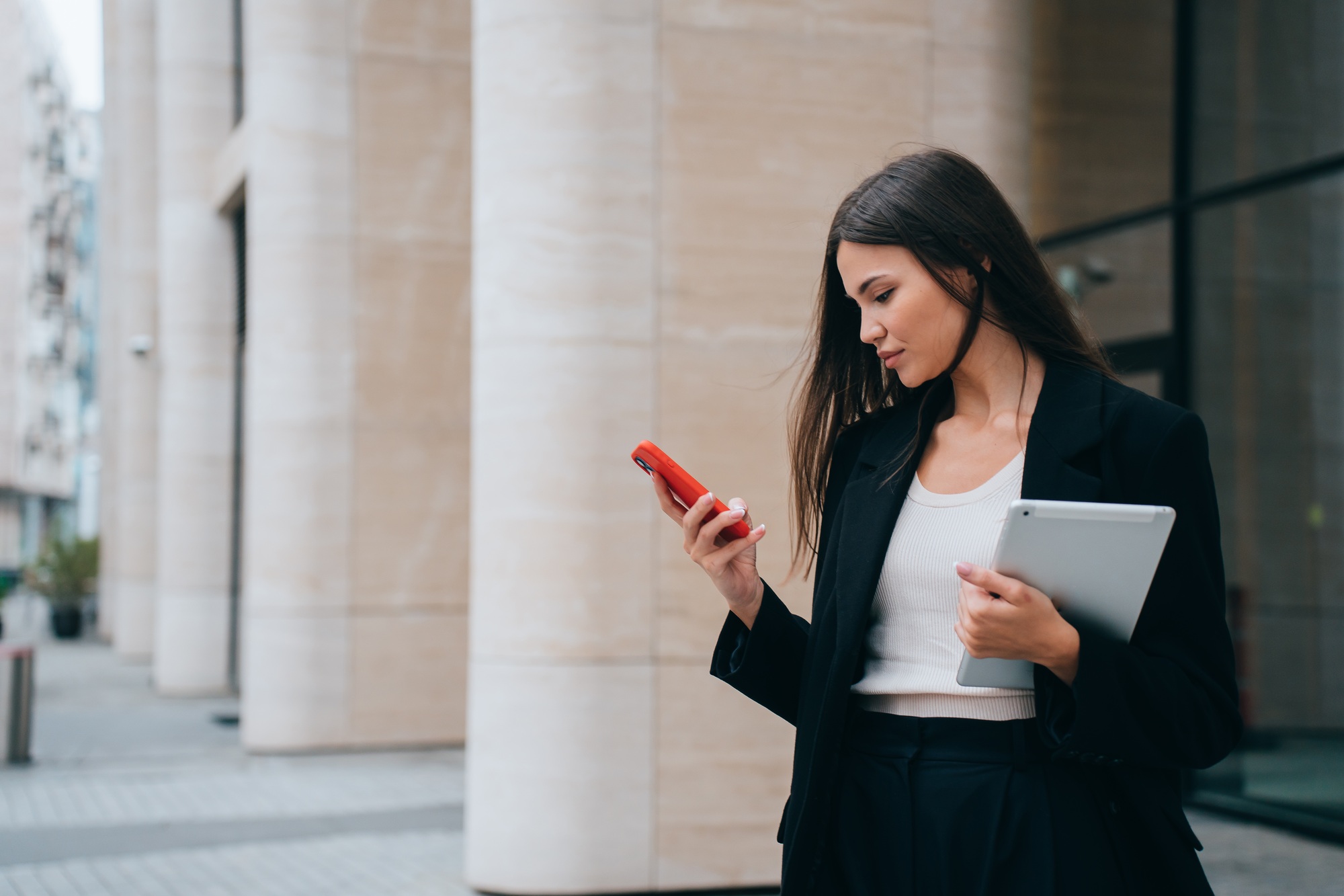 successful girl, lawyer stands outside courthouse, reads messages on phone, holds tablet and studies