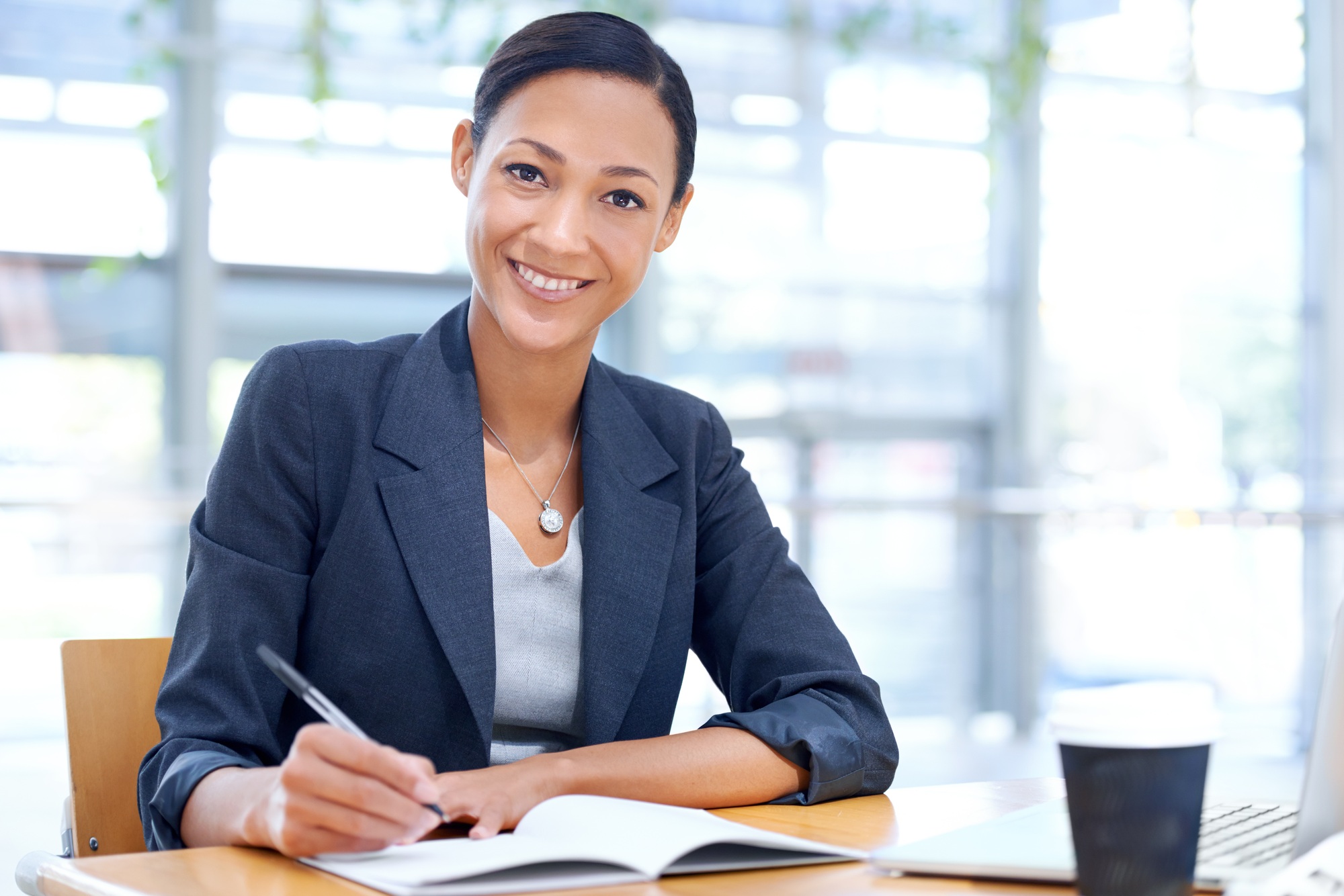 Taking minutes for the meeting. A businesswoman writing on a notebook while sitting in her office.
