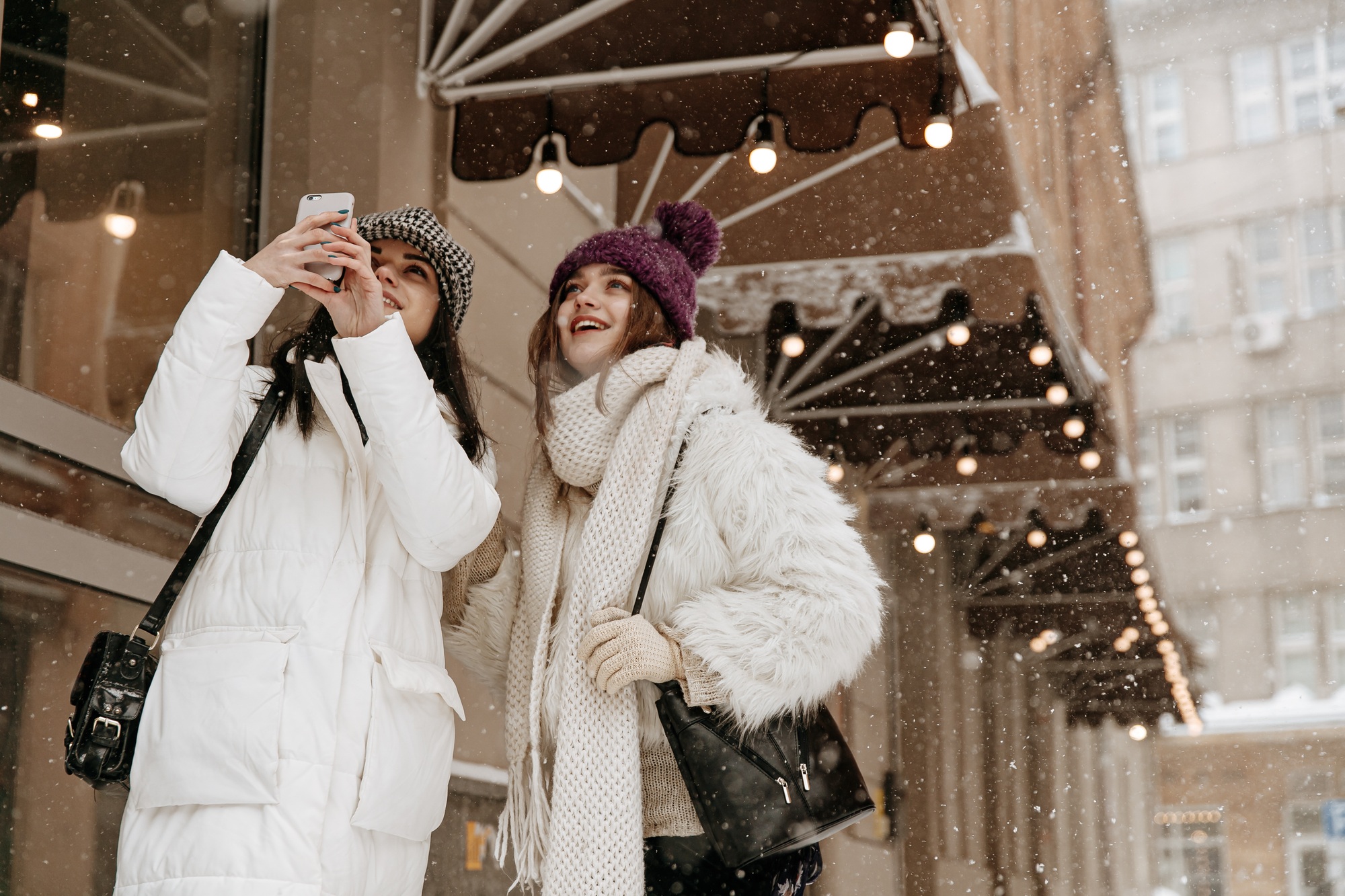 Two cheerful women doing pictures of falling snow on mobil