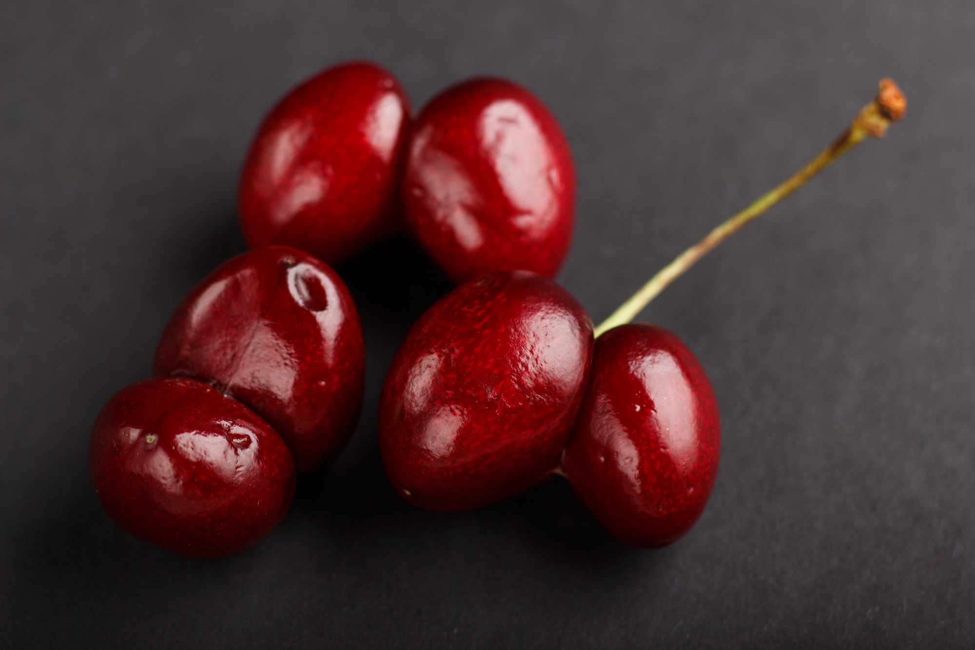 Ugly weird red sweet cherry on black background. side view.