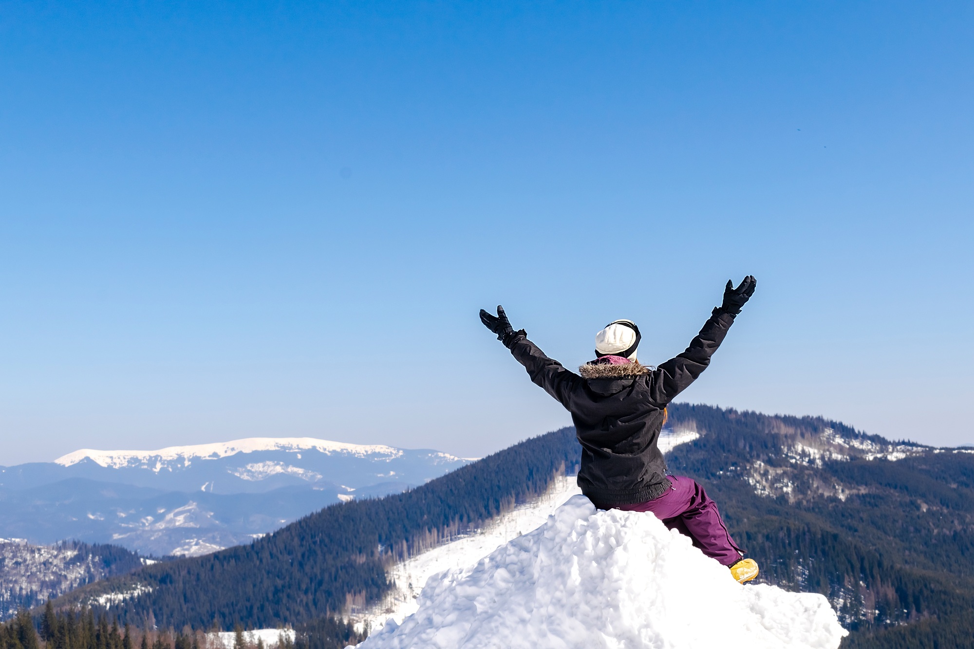Women alpine girl sitting on snow hill looking at snow high mountains at winter ski resort,landscape