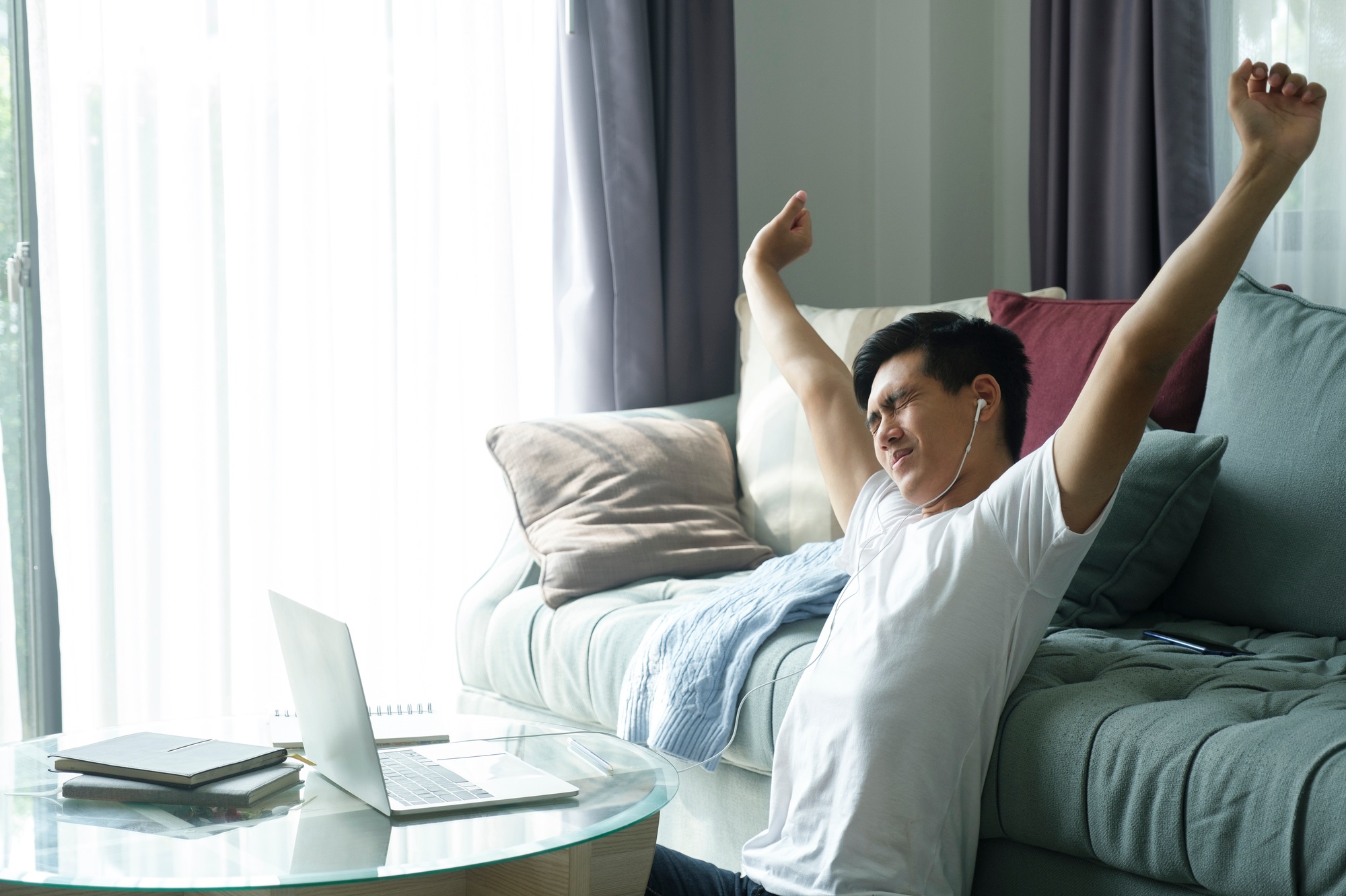 Young businessman sitting at home working at his desk hands up and stretching his arms.