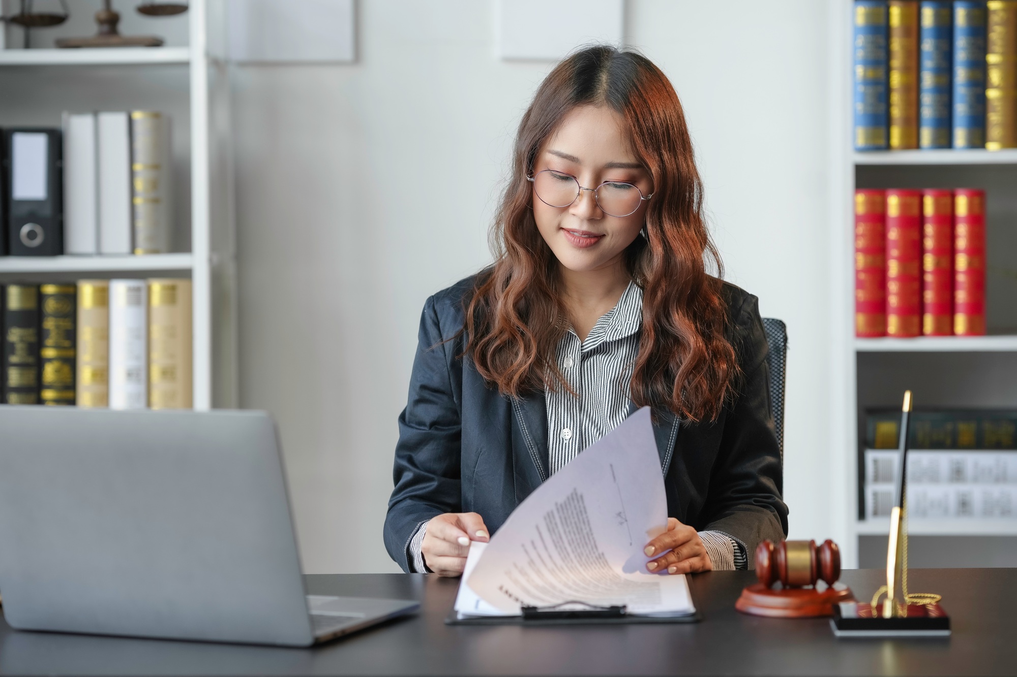 Young lawyer focused on legal documents in office, surrounded by law books and paperwork