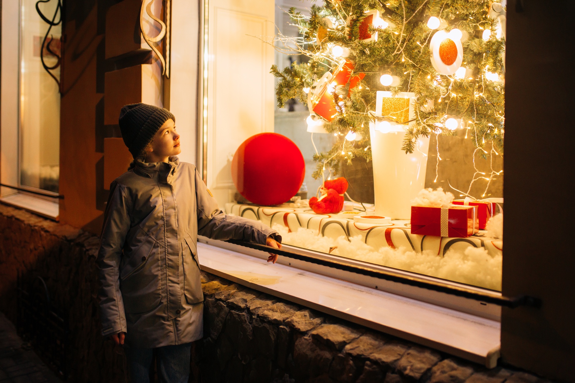 A girl stands near a showcase in which a Christmas tree is displayed in New Year's windows