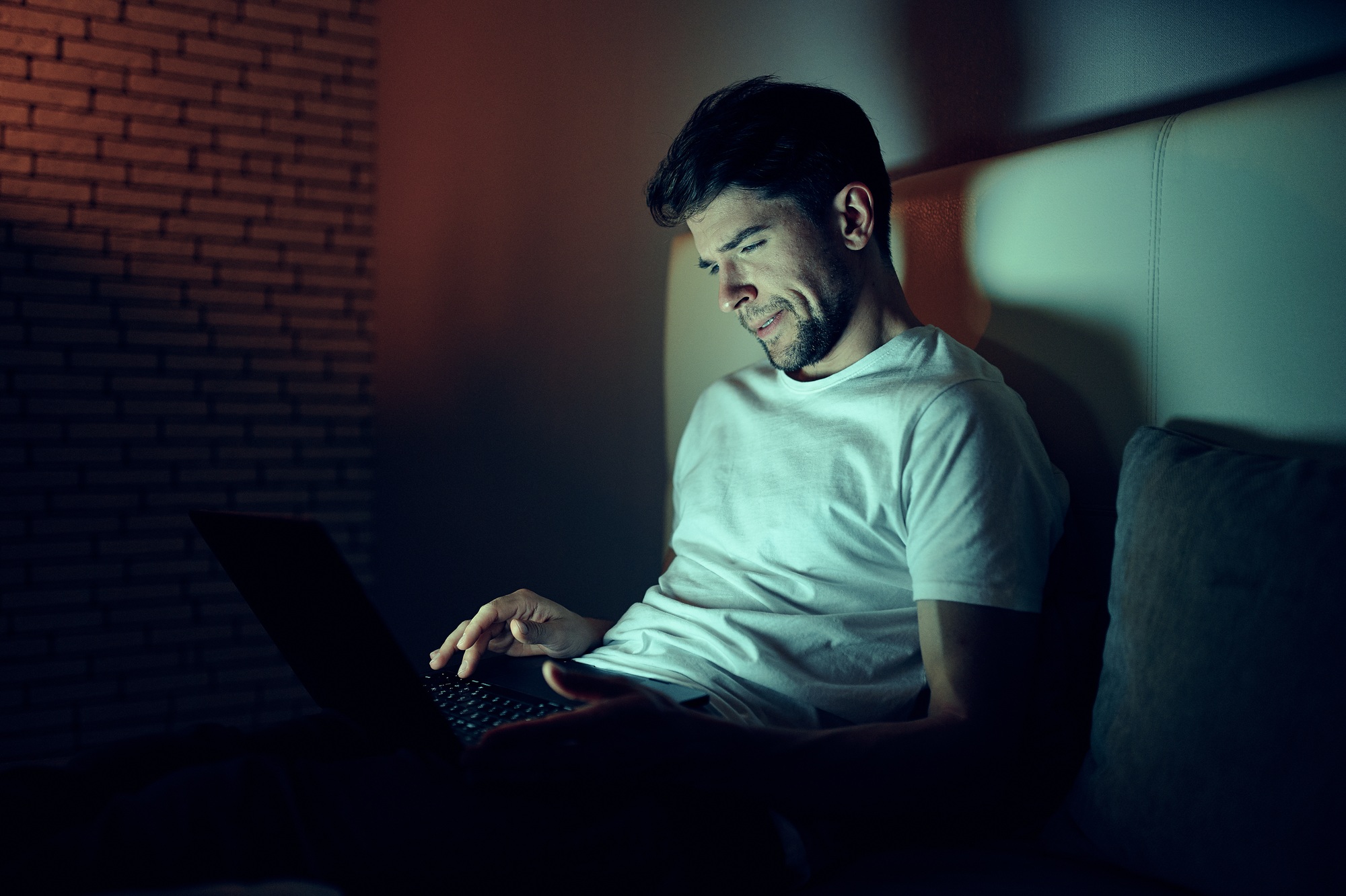 A man indoors at night prints text on a laptop