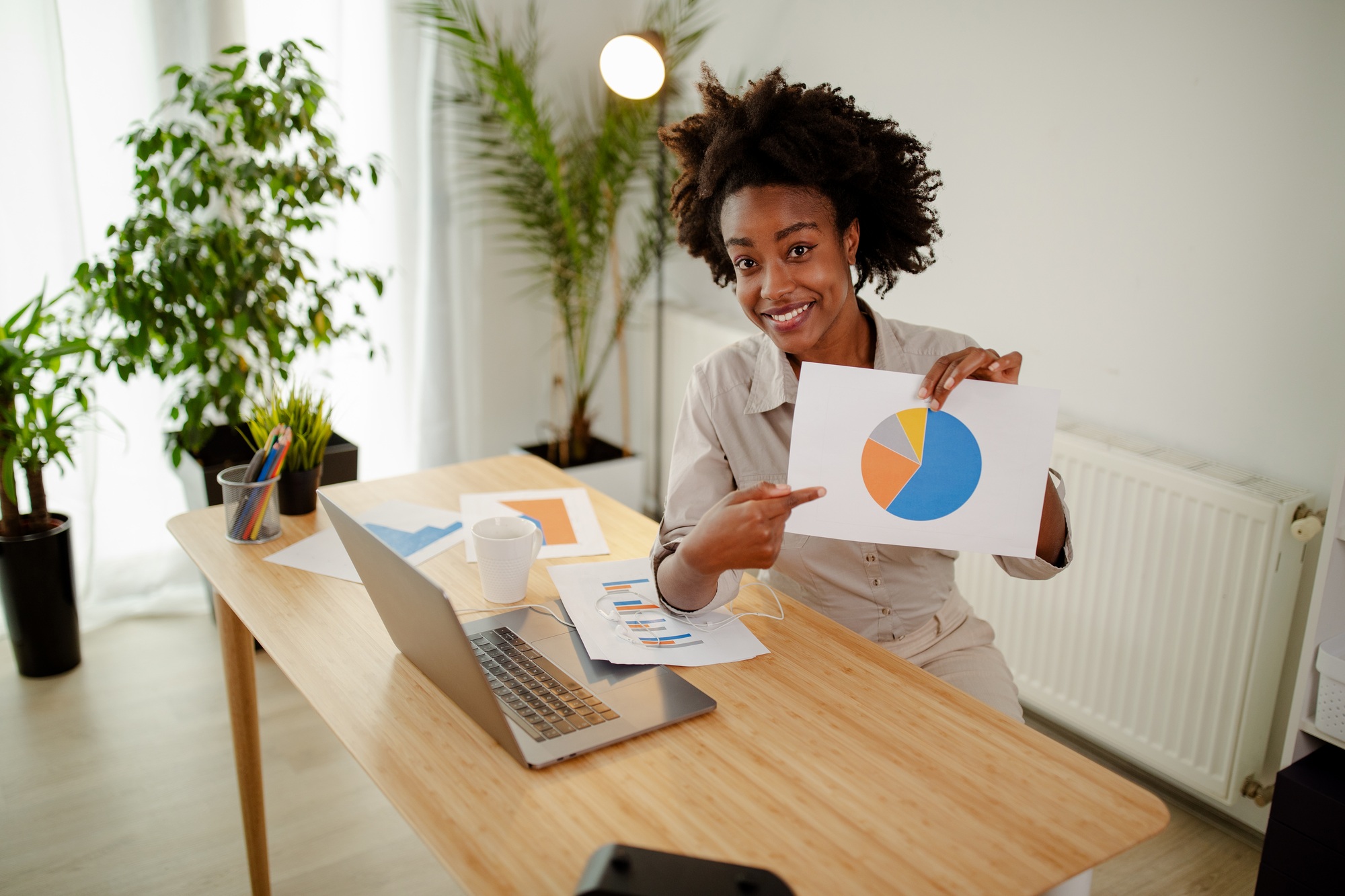 Afro American businesswoman showing business diagram at paper while looking at camera and smiling.