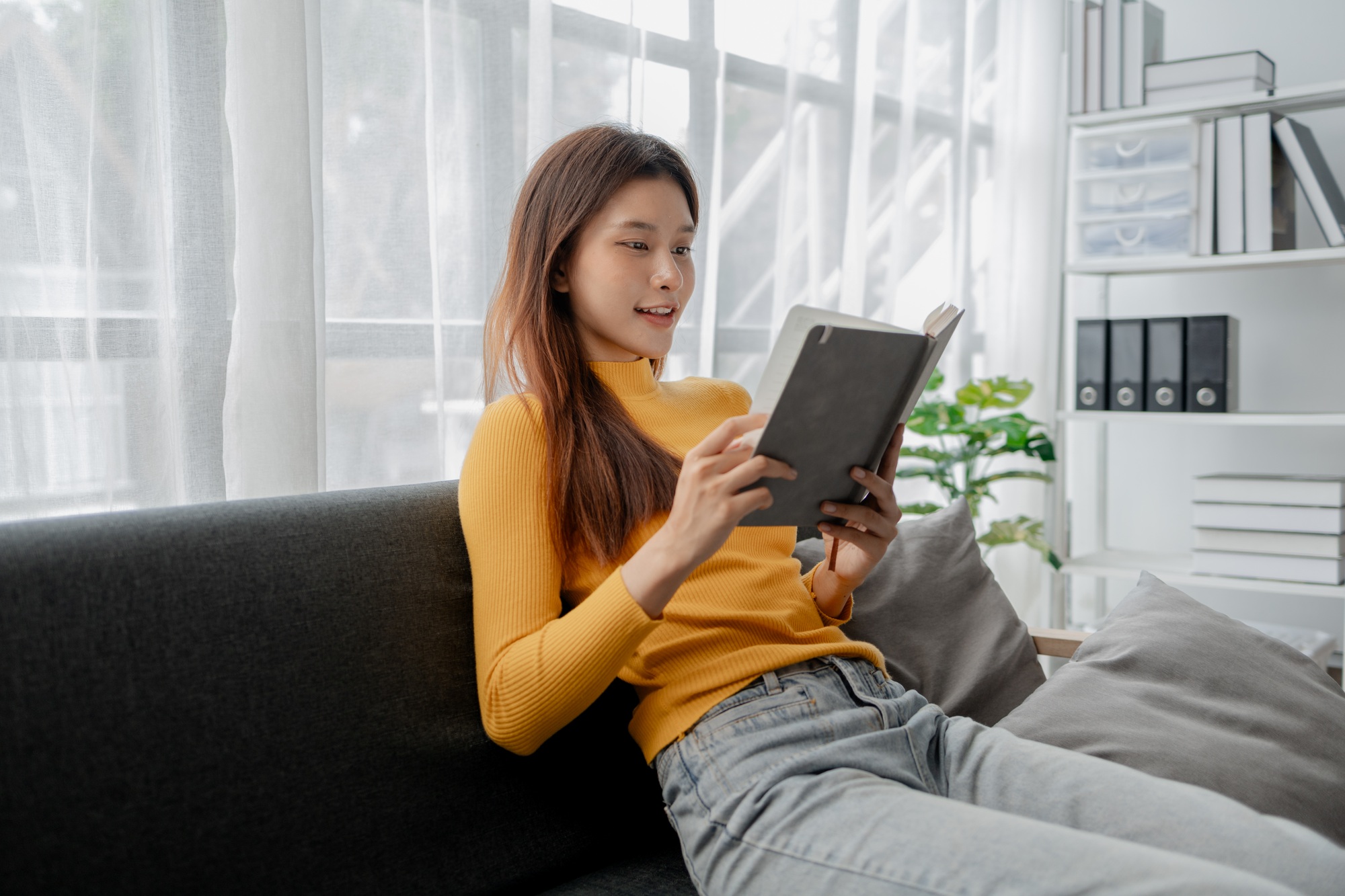 Asian woman in the living room and reading a book, female company employee on vacation, using vacati