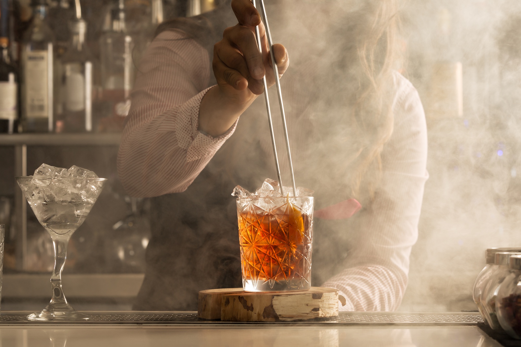 Bartender with tongs adding ingredient into cocktail