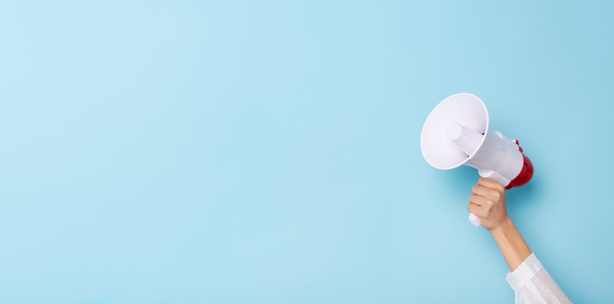 Business Hand holds a megaphone from a hole in the wall on blue background.  hiring, advertising,