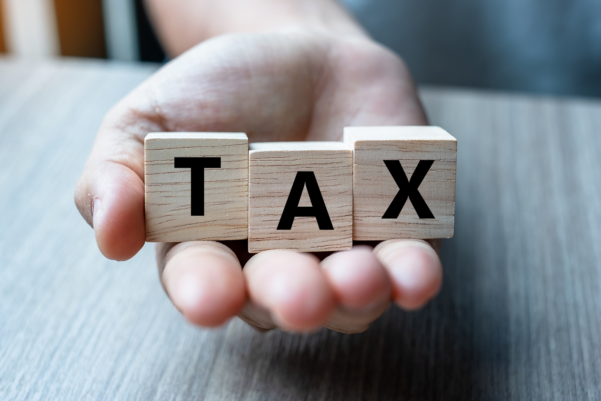 Business woman hand holding wooden cube with TAX text on table background.