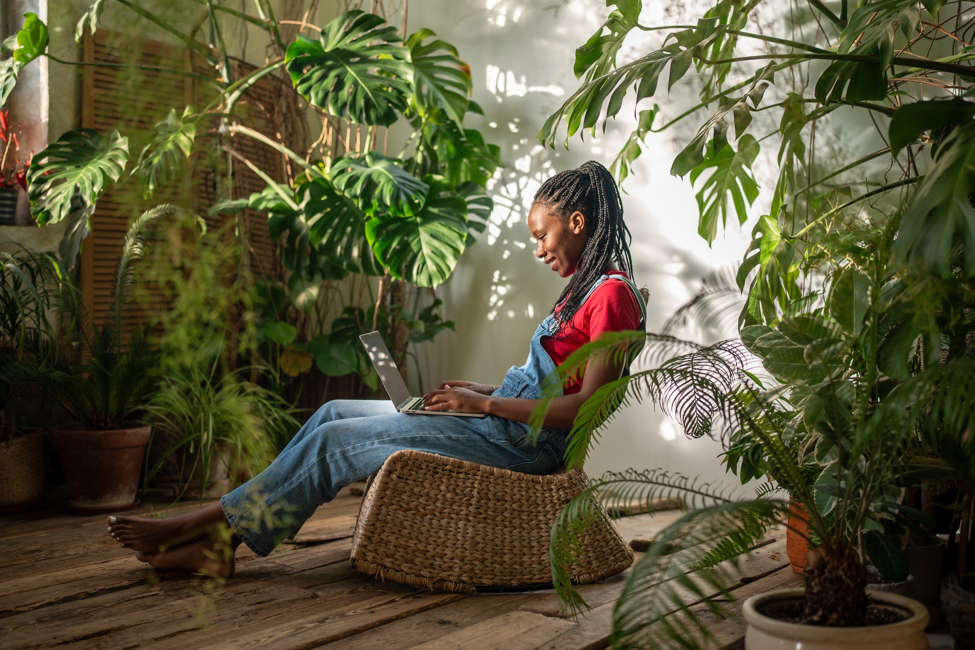 Calm smiling black woman works on laptop among plants, managing small flower business. Home office