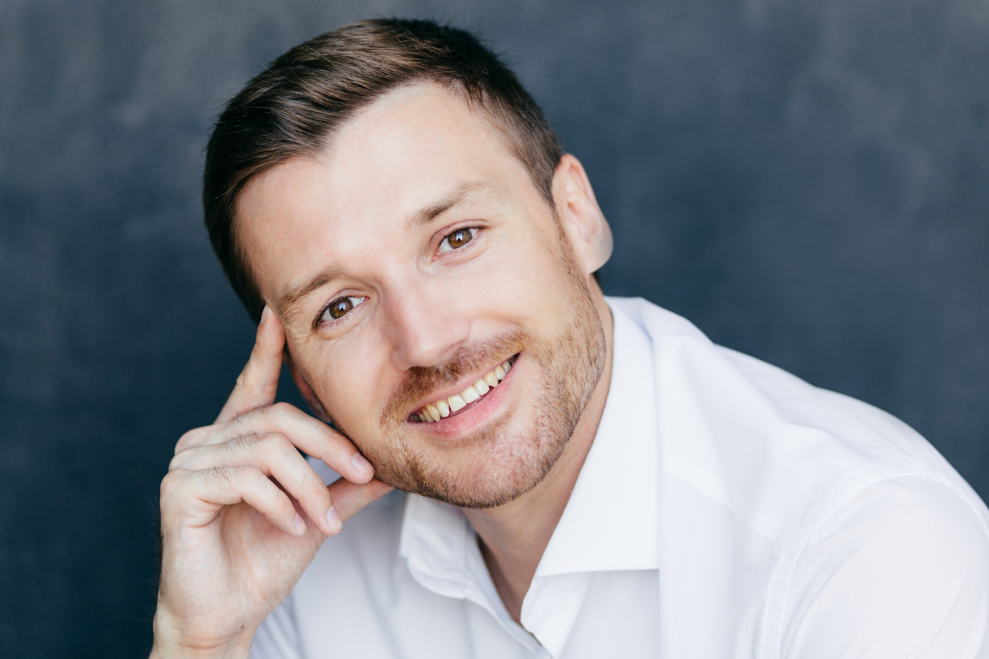 Cheerful male employee has joyful expression, keeps finger on temple, rejoices starting vacation