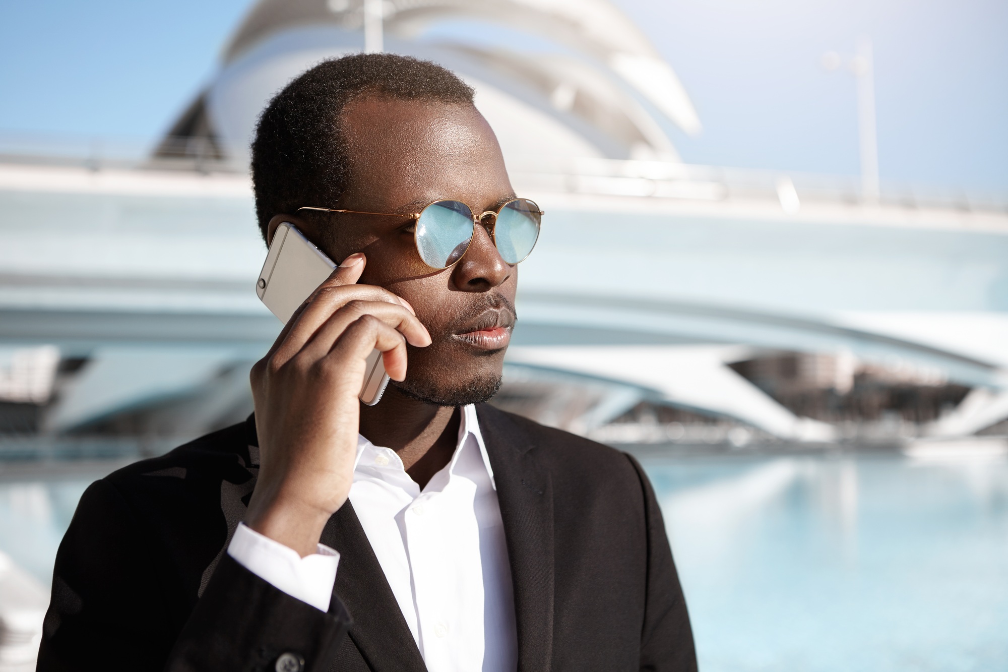 Confident young black European businessman having business negotiations on cell phone, making appoin