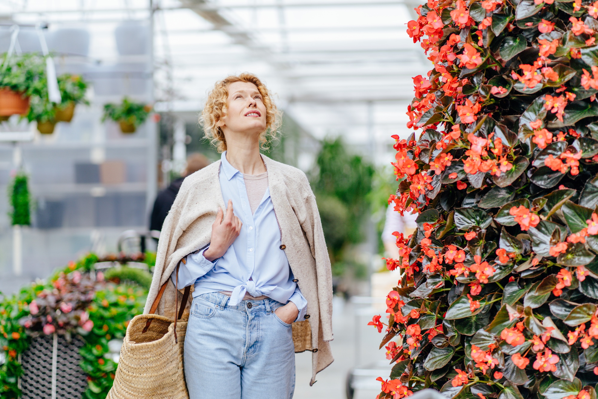 Confused blond woman customer in front of a huge selection of flowers in a garden center.