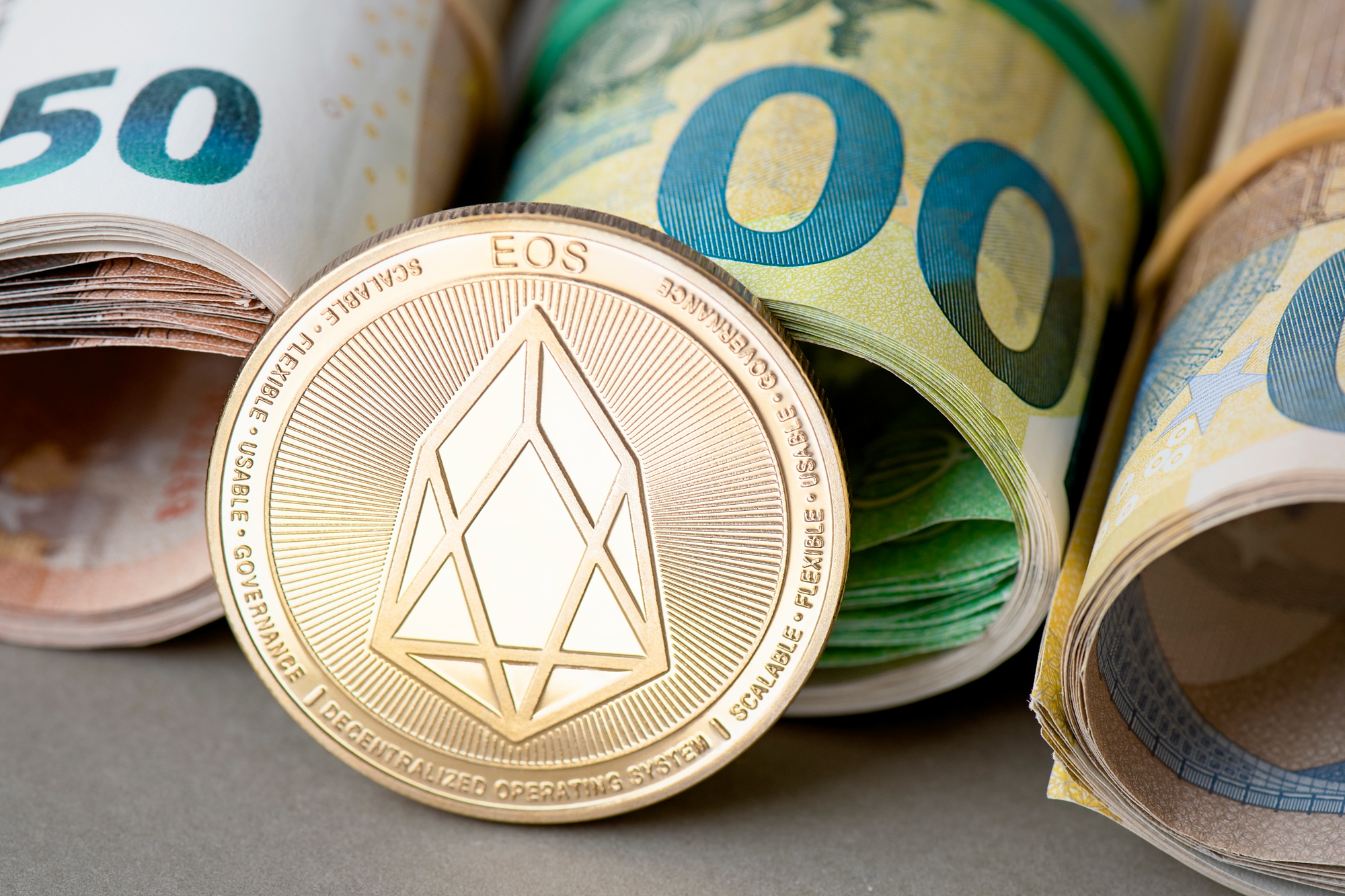 Cryptocurrency EOS golden coin on the background of rolled euro bills.