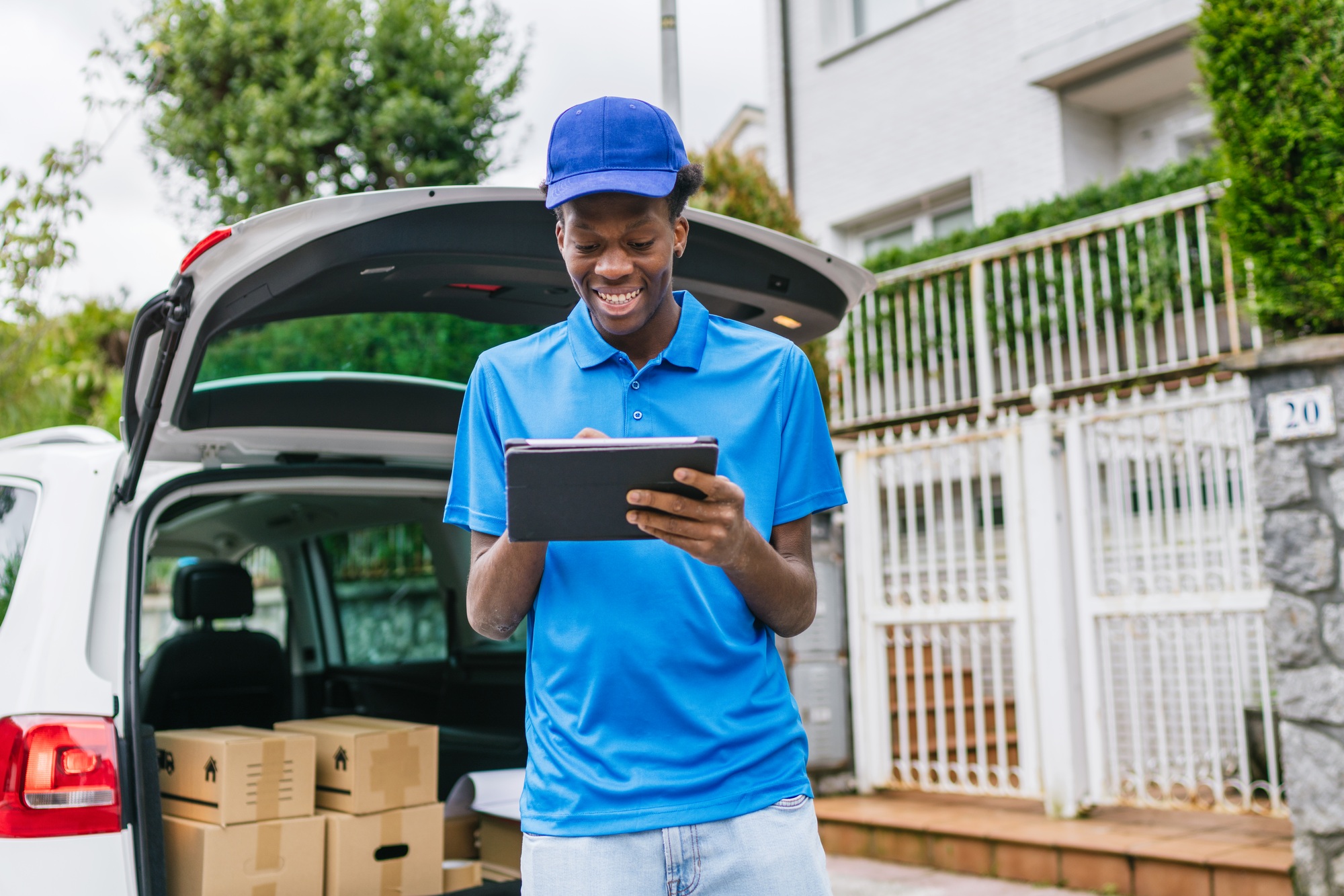 Delivery worker using a tablet to track packages near a vehicle full of boxes.