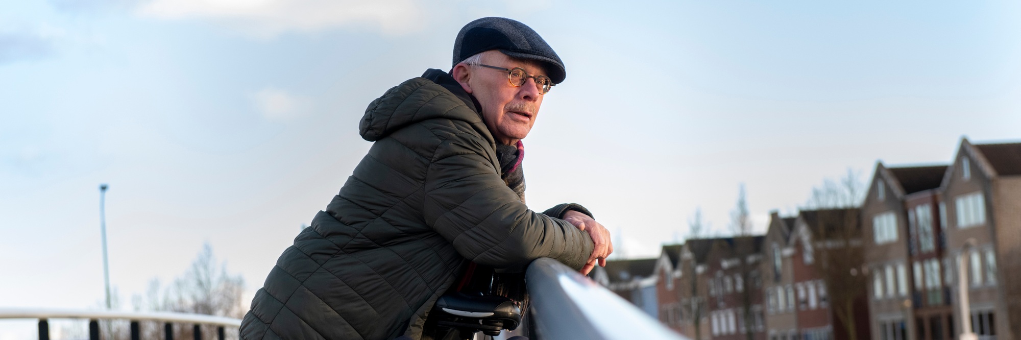 Elderly man going for a healthy walk and leaning on a railing looking at the landscape