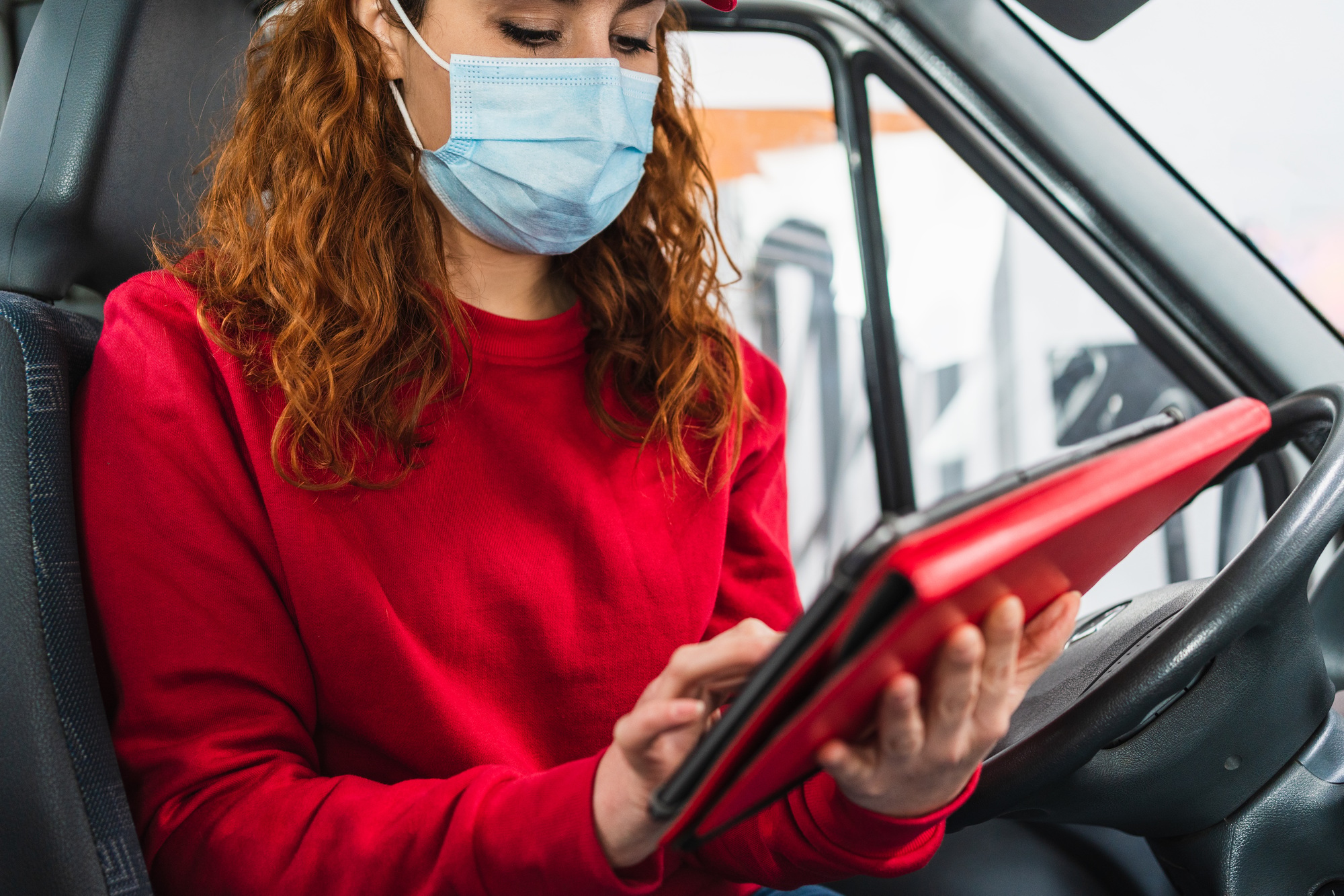 Female delivery driver with a medical mask tracking a package on her tablet