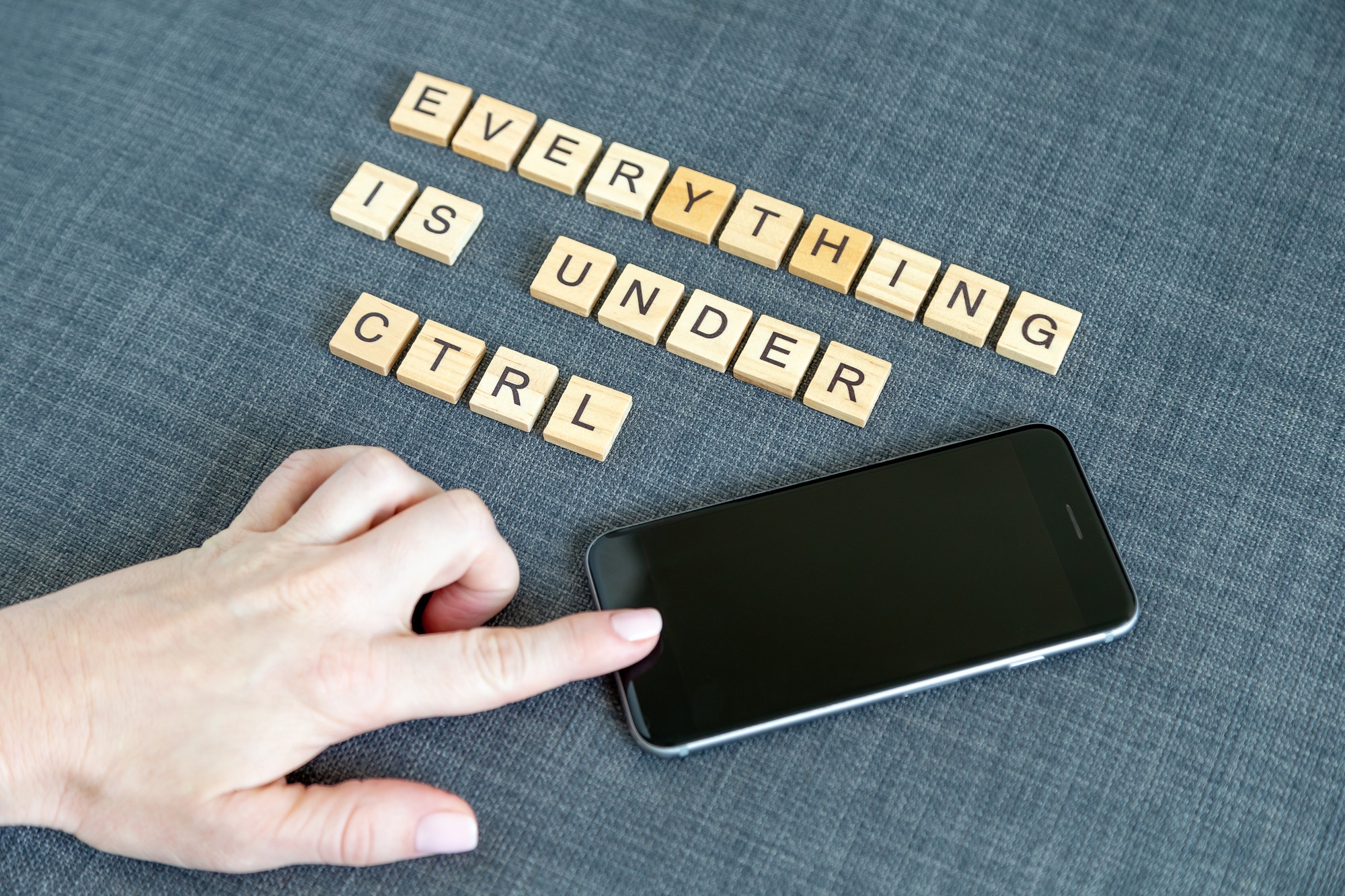 Female hand pressing mobile phone button. Text made with wooden blocks “Everything is under control”