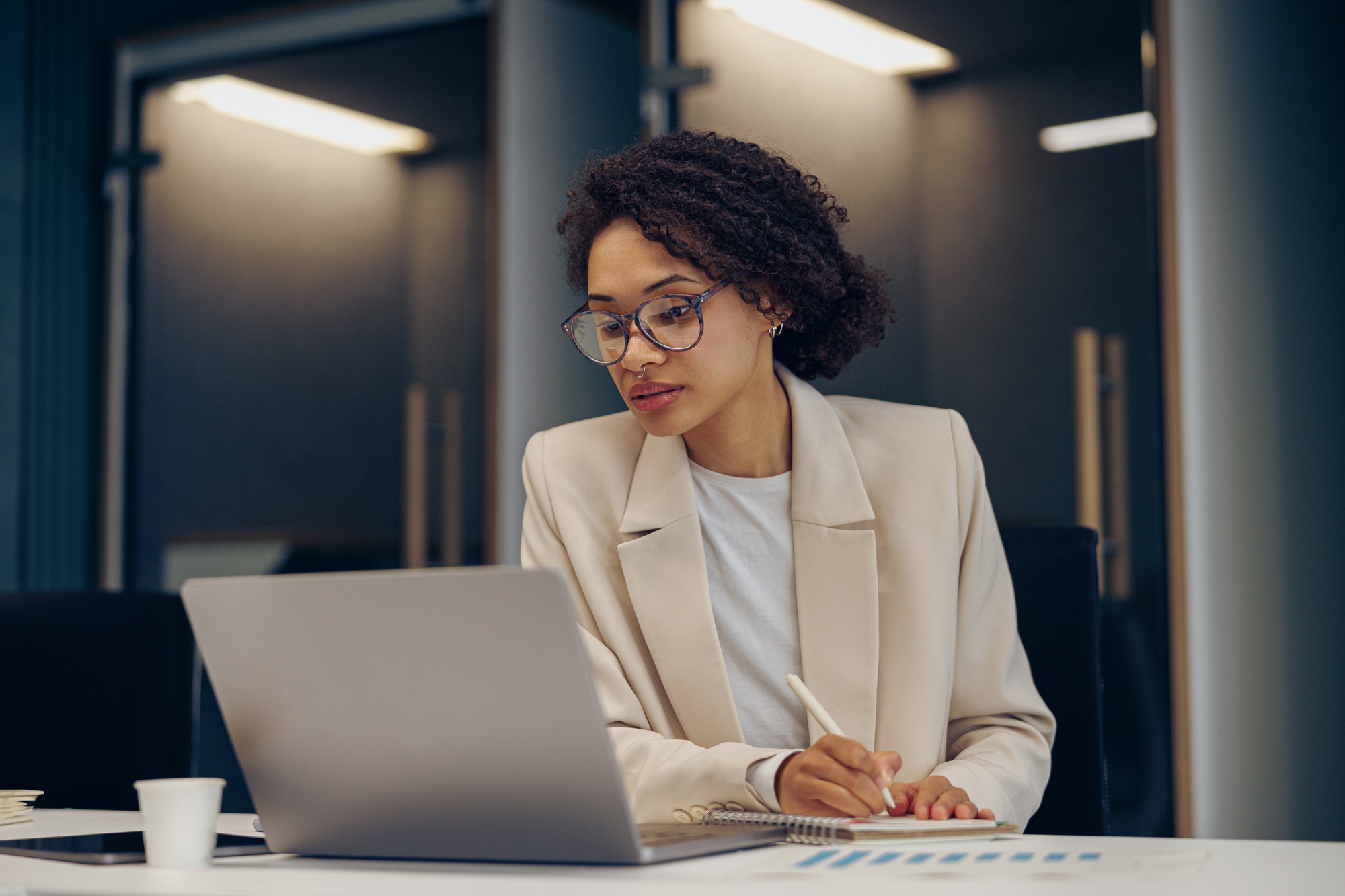 Focused female freelancer in eyeglasses working on laptop while sitting in modern coworking
