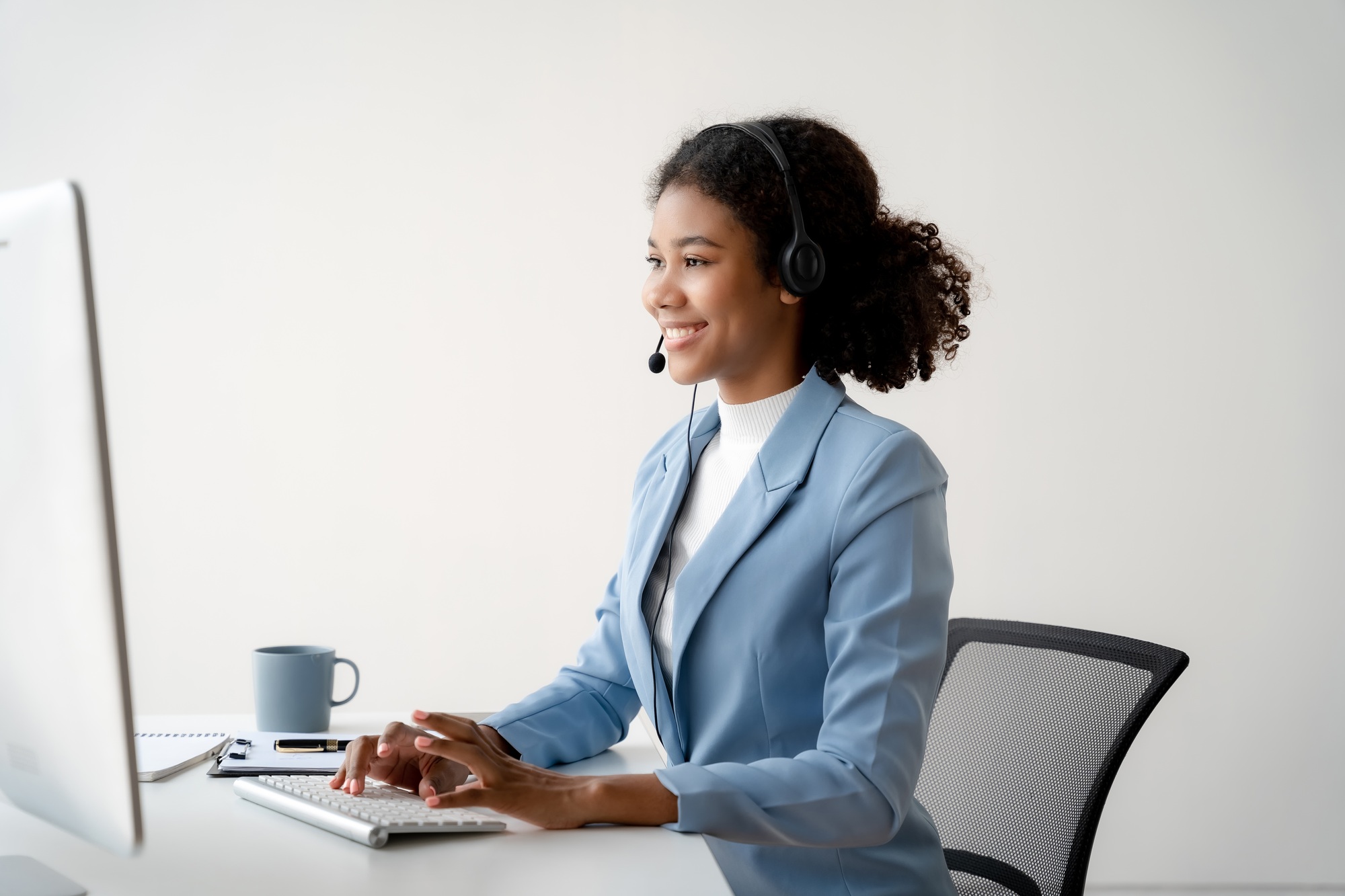 Friendly smiling female call-center agent with headset working on support hotline in office.