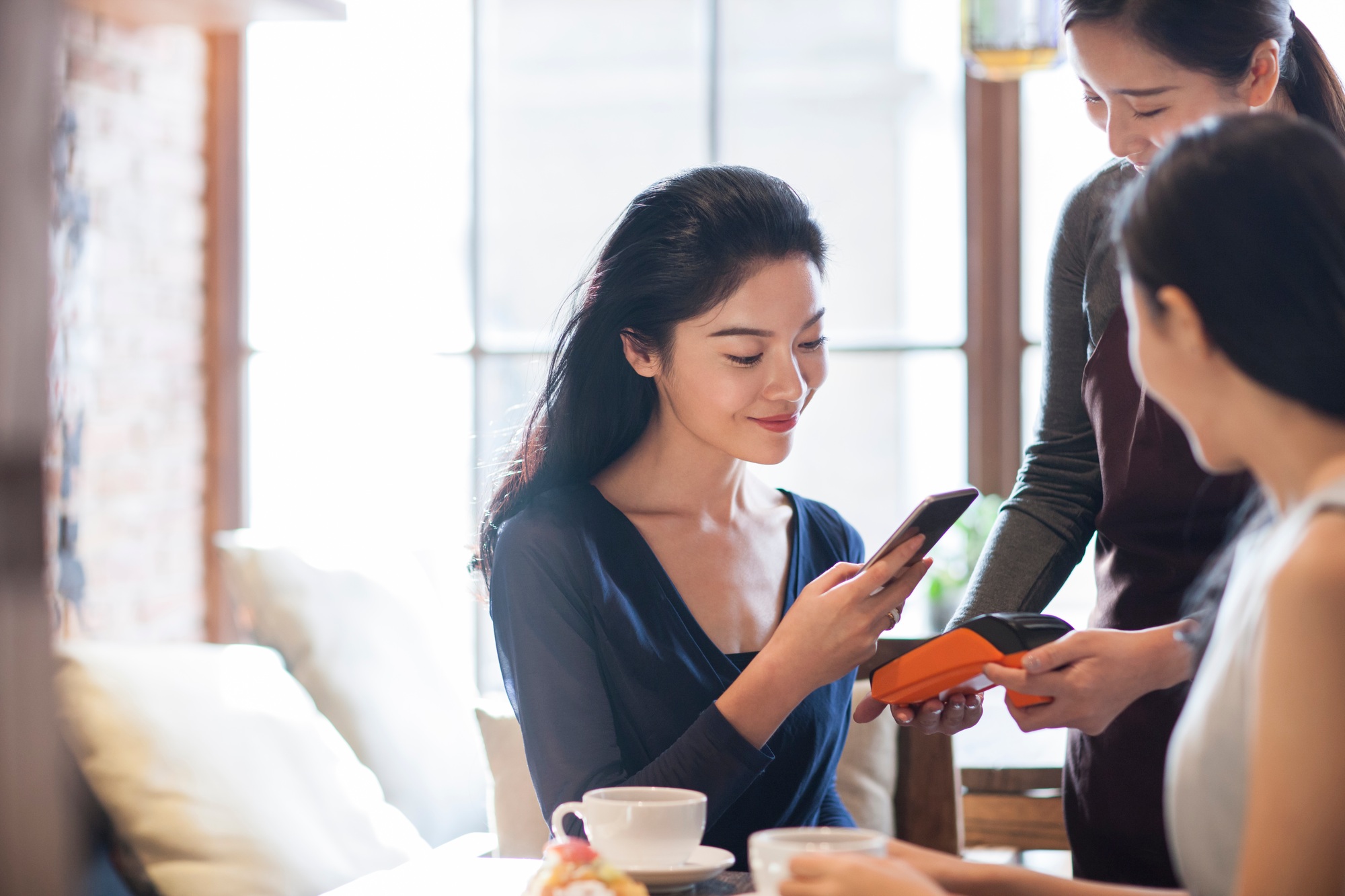 Friends paying with smart phone in café