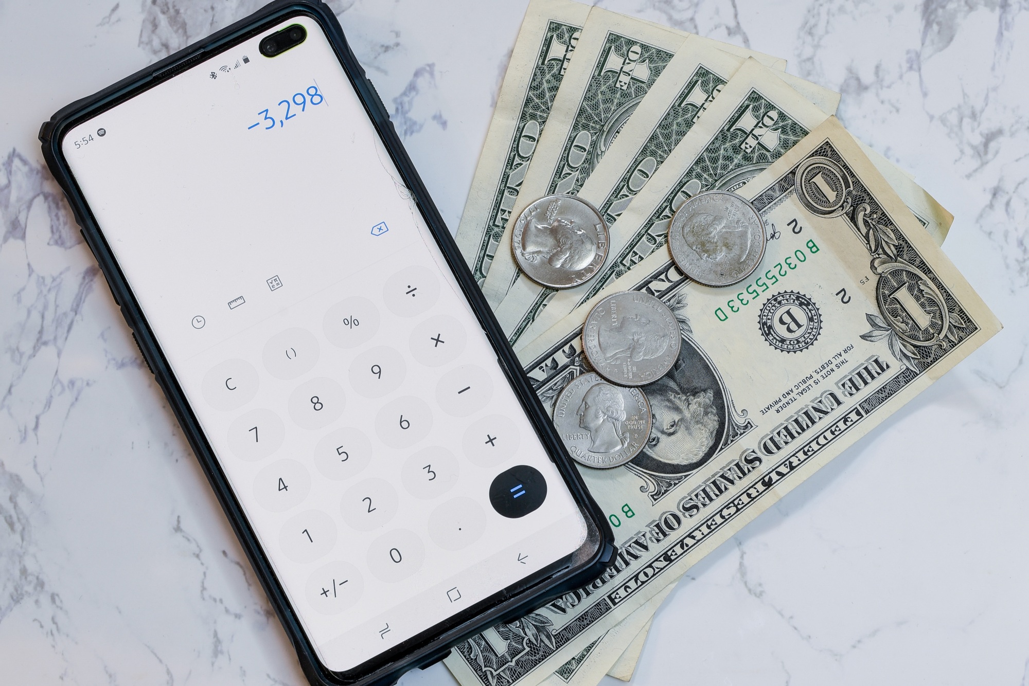 High angle view of a phone with the calculator app on it on dollars and coins on the table